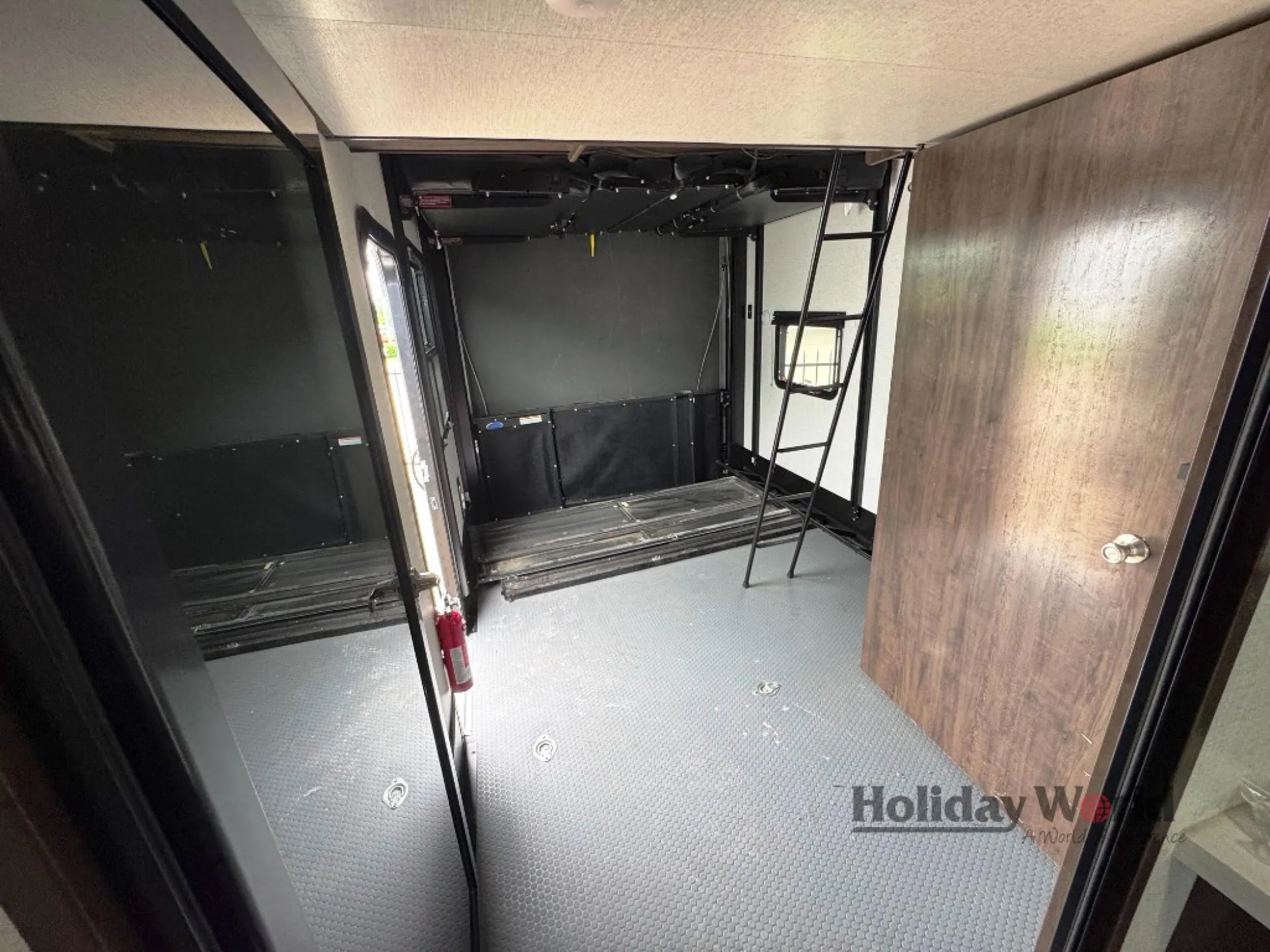 2022 Dutchmen Voltage 4225 — Fifth-wheel toy-hauler garage with a broad textured cargo floor, ramp-side walls, overhead bed hardware, and ladder