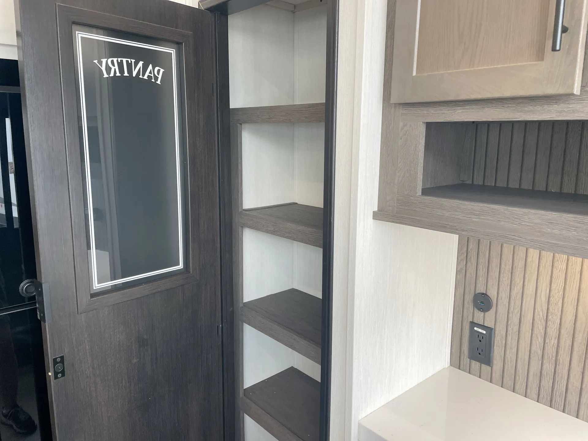 2026 Forest River Arctic Wolf 38LEAH.G — Open tall pantry cabinet with multiple shelves beside a countertop, outlet, and wall cabinetry