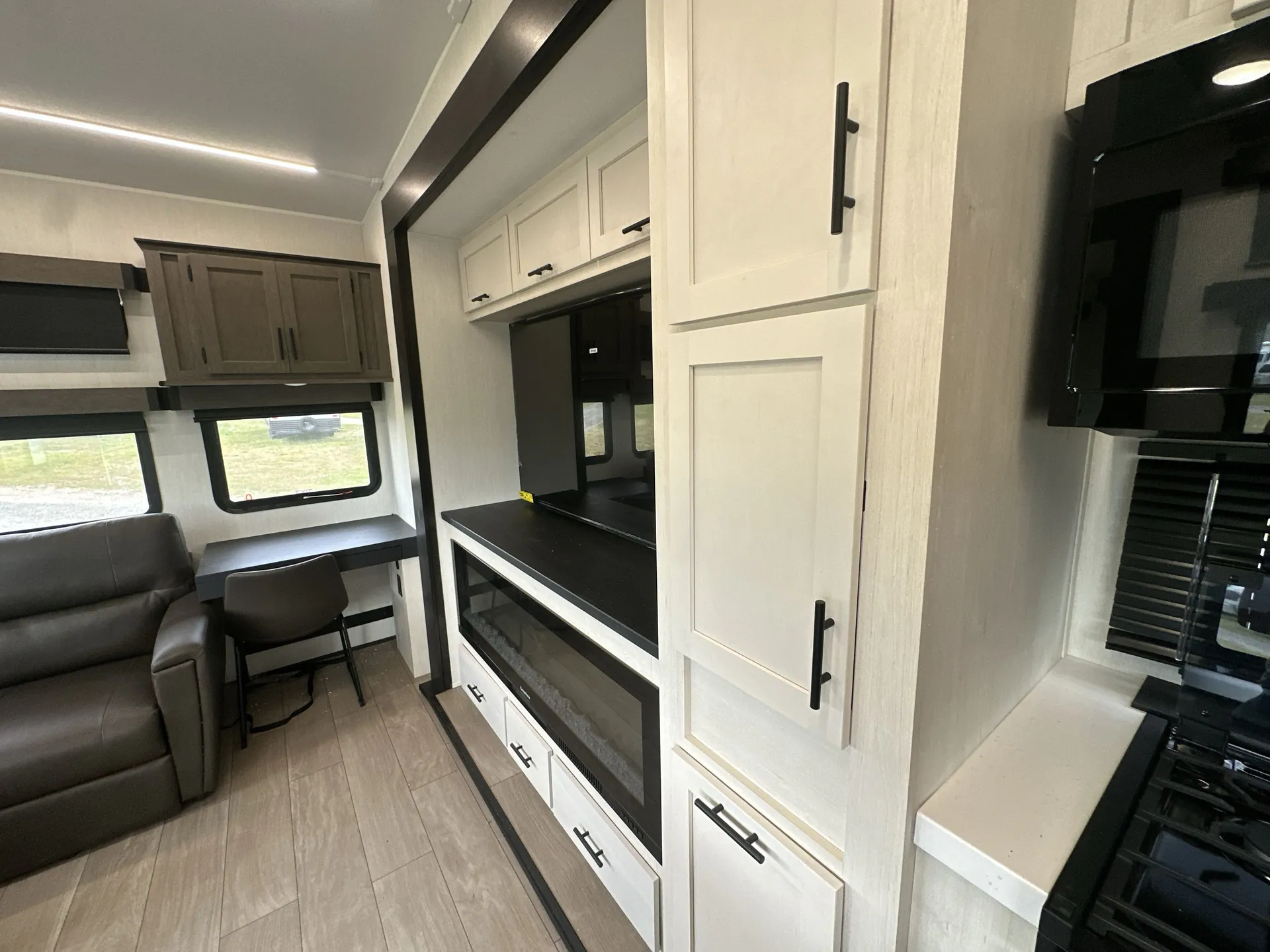 2026 Forest River Arctic Wolf 38LEAH.G — Living room seating and desk appear beside a media fireplace wall and adjacent kitchen range and cabinetry