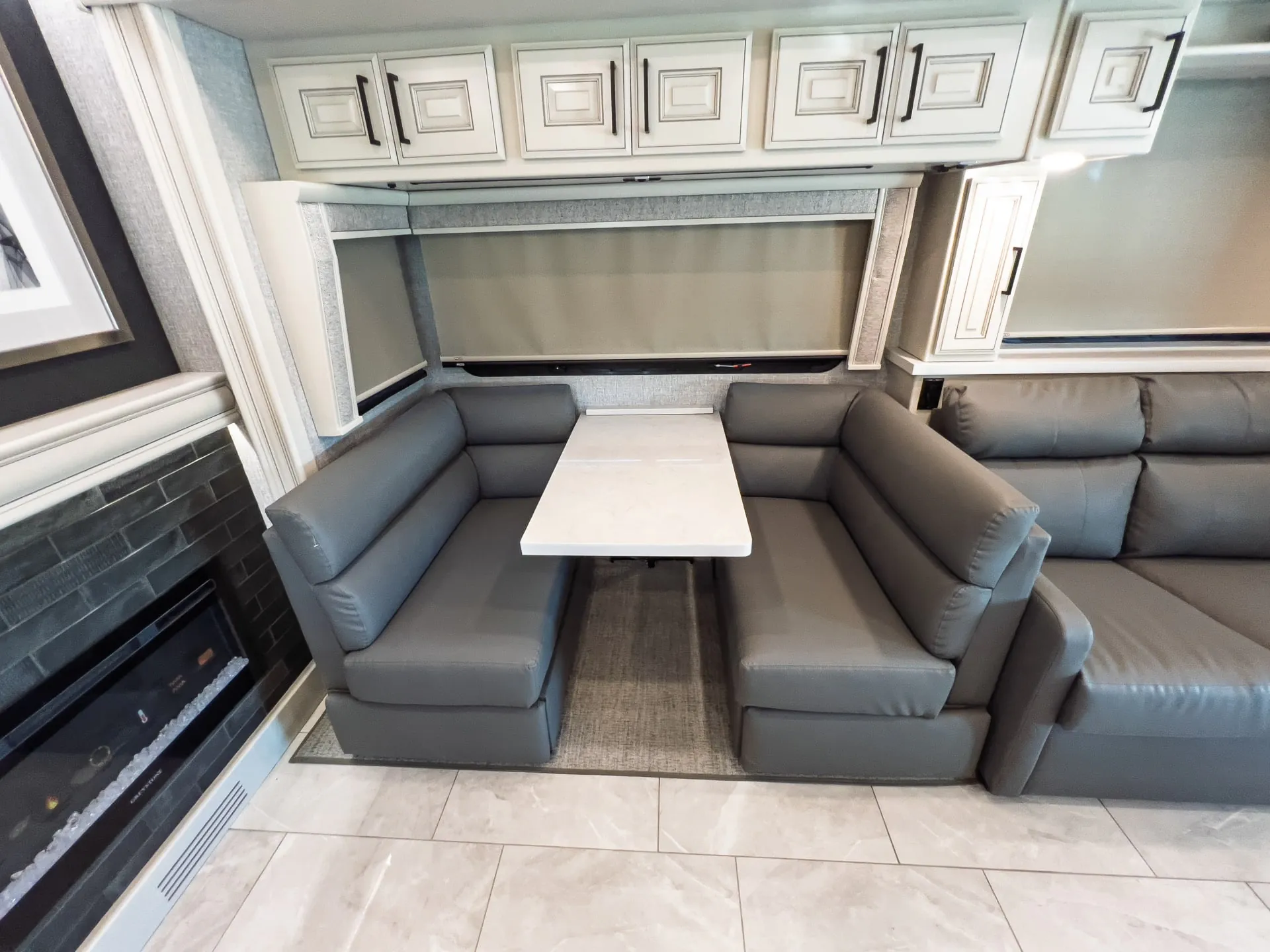 2027 Fleetwood Discovery LXE 40M — U-shaped dinette with table beside a lounge sofa, fireplace, and overhead cabinetry