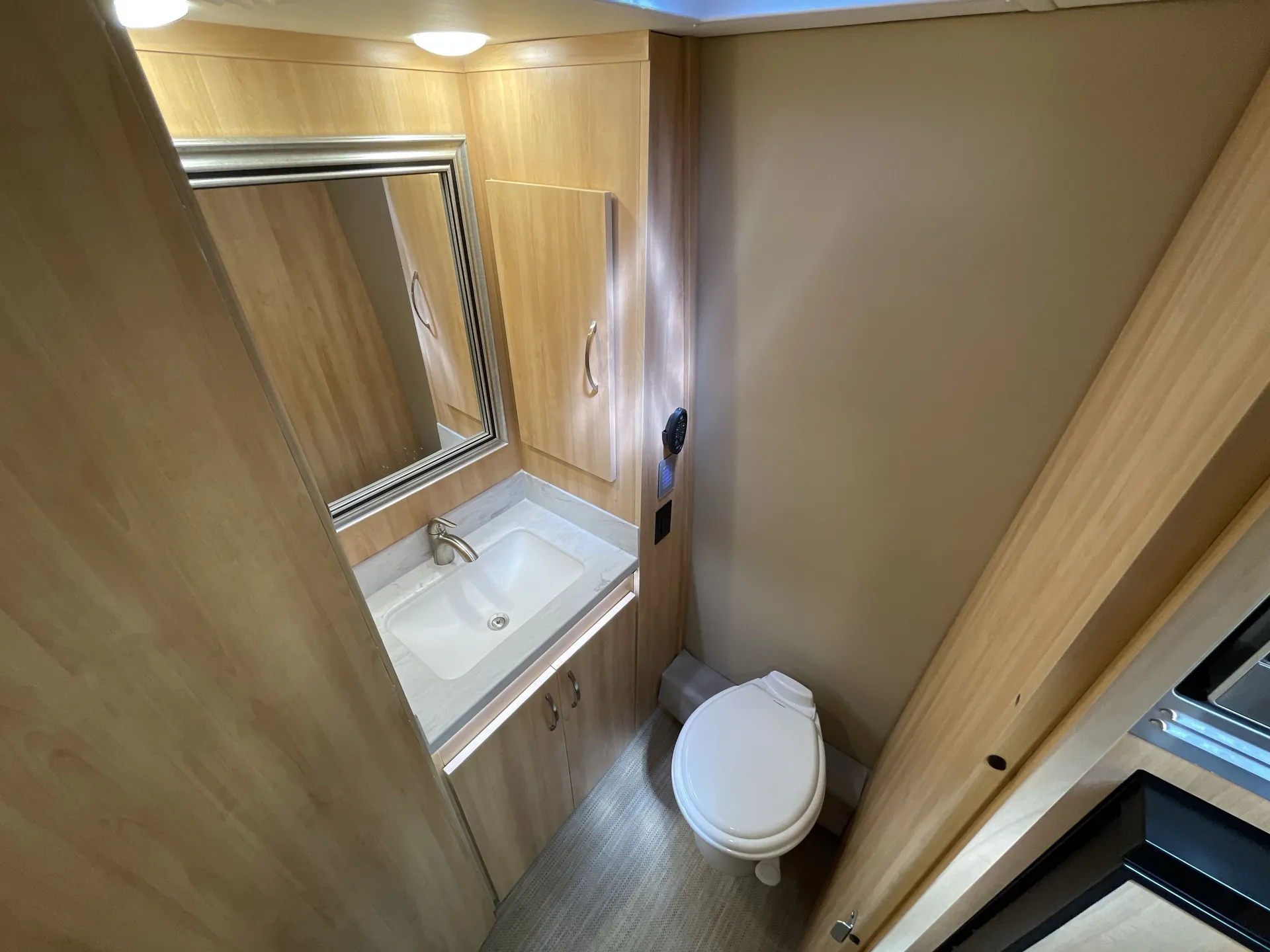 2024 Chinook RV Maverick SS — Compact bathroom with toilet, sink vanity, mirror, wood cabinetry, and a narrow interior layout