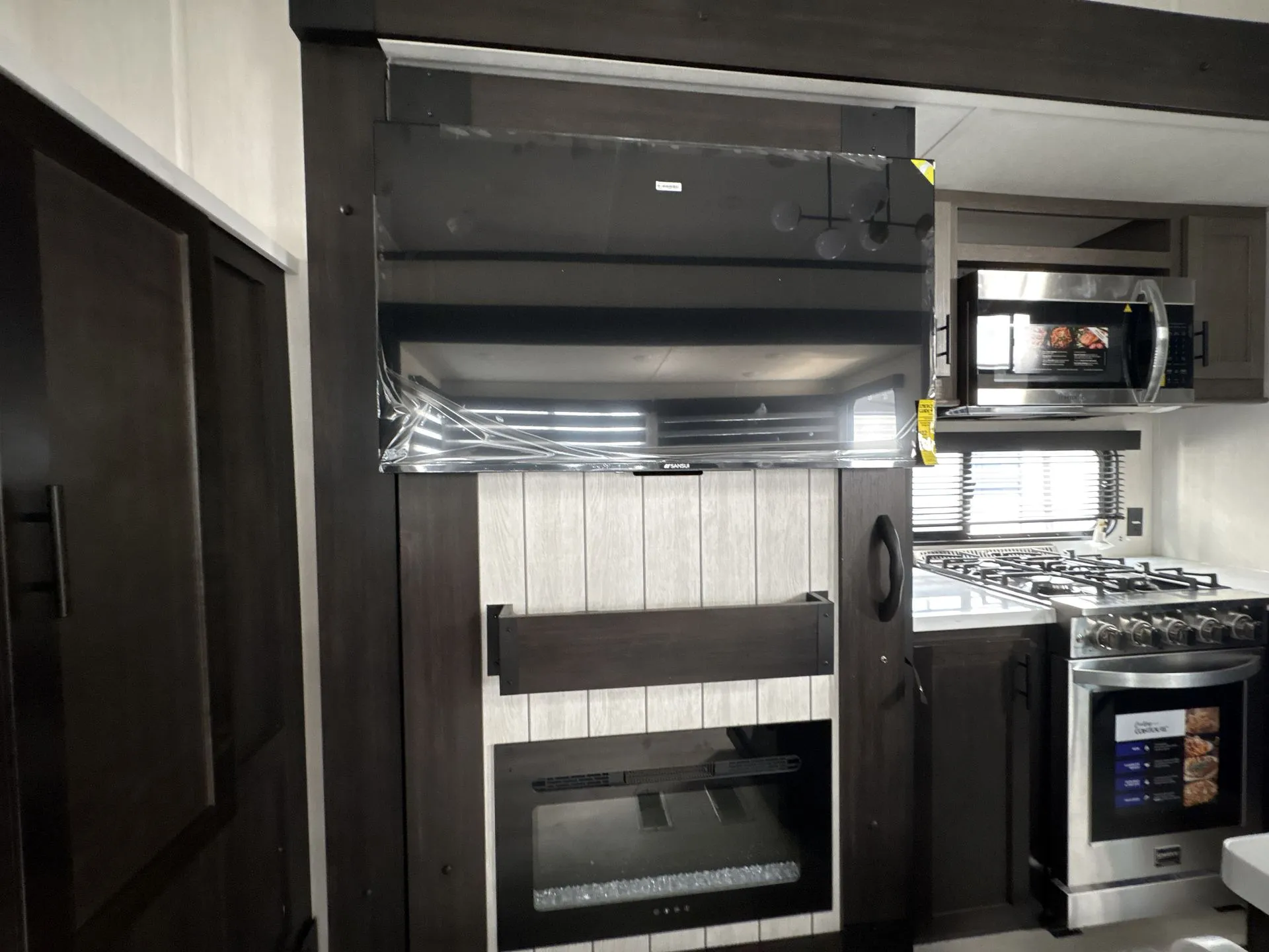 2026 Forest River Cherokee Wolf Pack 397STAY — Travel trailer kitchen with refrigerator, range, microwave, and dark cabinetry surrounding a fireplace