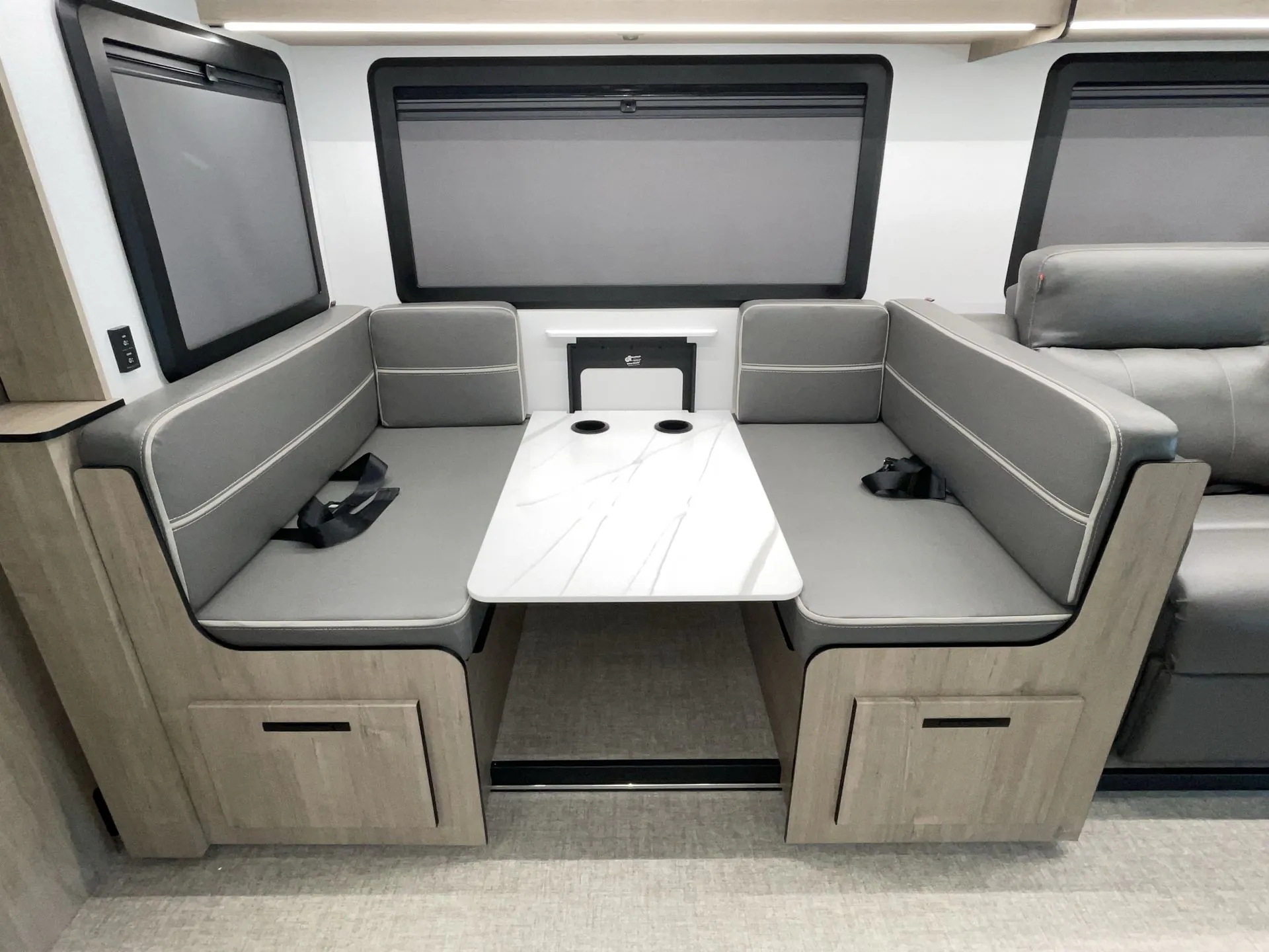 2027 Grand Design Lineage Series F 31ZW — RV dinette with opposing upholstered benches, a white table, seat belts, windows, and lower storage cabinets