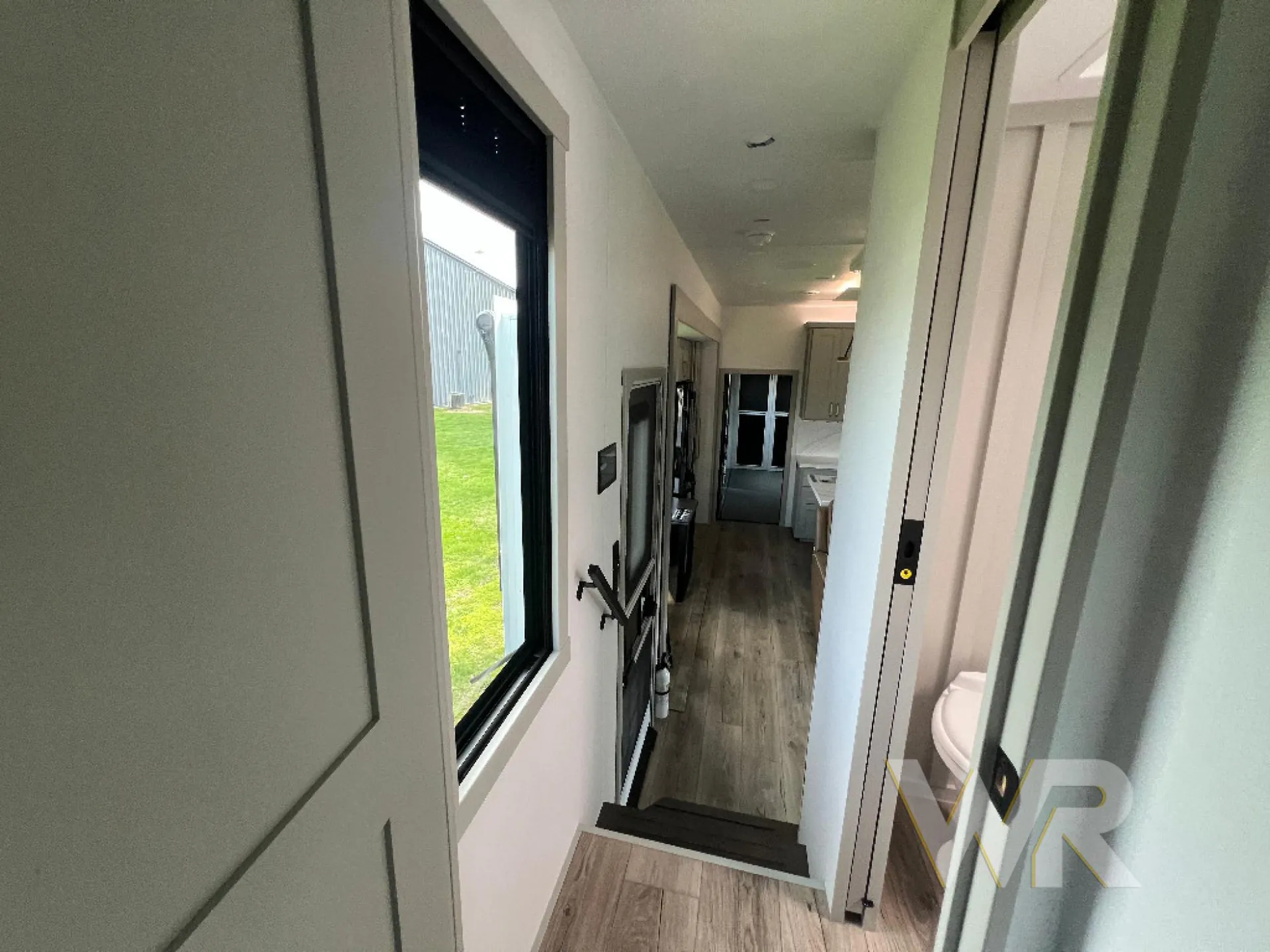 2026 Brinkley Model G 3950 — Fifth wheel interior hallway showing a step-down passage, wall-mounted television, kitchen at the far end, and open bathroom doorway