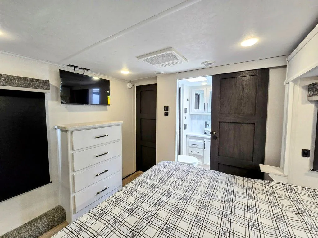 2025 Dutchmen Voltage 4225 — Bedroom view showing a large bed, dresser with television, windows, and bathroom doorway