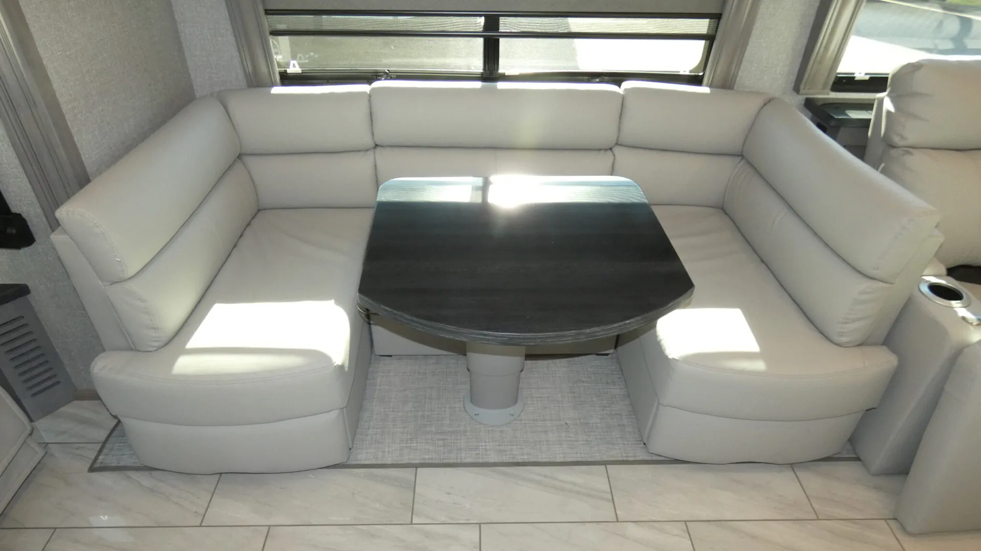 2026 Fleetwood Discovery LXE 40G — U-shaped dinette with upholstered bench seating, central pedestal table, window, and overhead cabinets