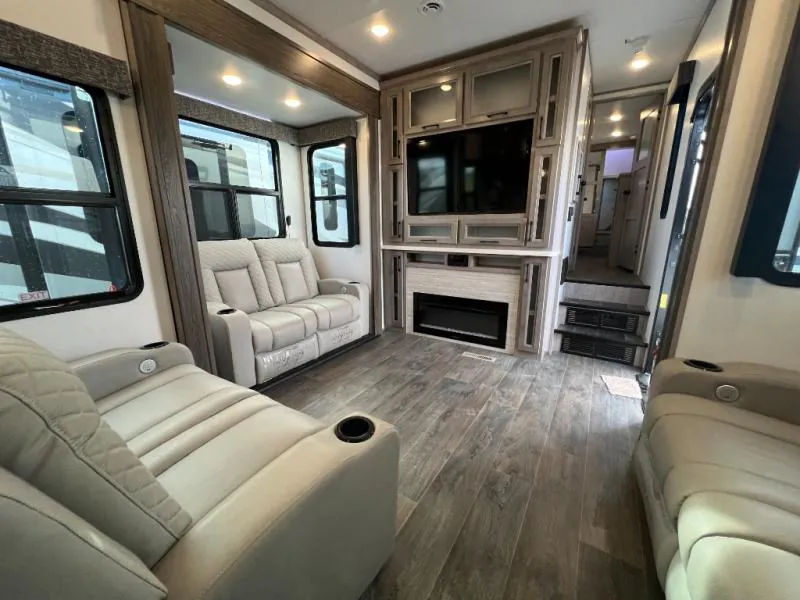 2023 Dutchmen Voltage 4225 — Fifth wheel living area with recliners facing a built-in television, fireplace, storage cabinetry, and hallway