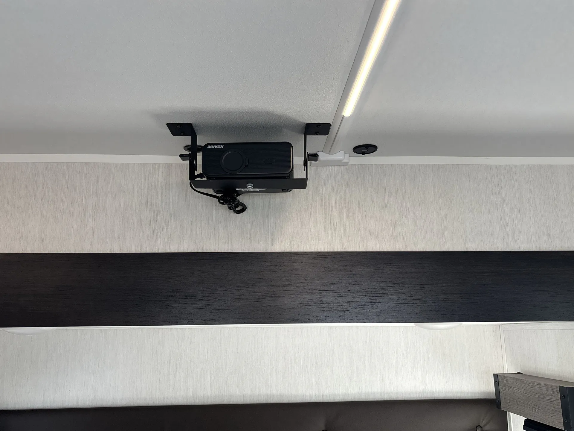 2026 Forest River Arctic Wolf 38LEAH.G — Ceiling-mounted projector above dark wall paneling with an illuminated linear light strip