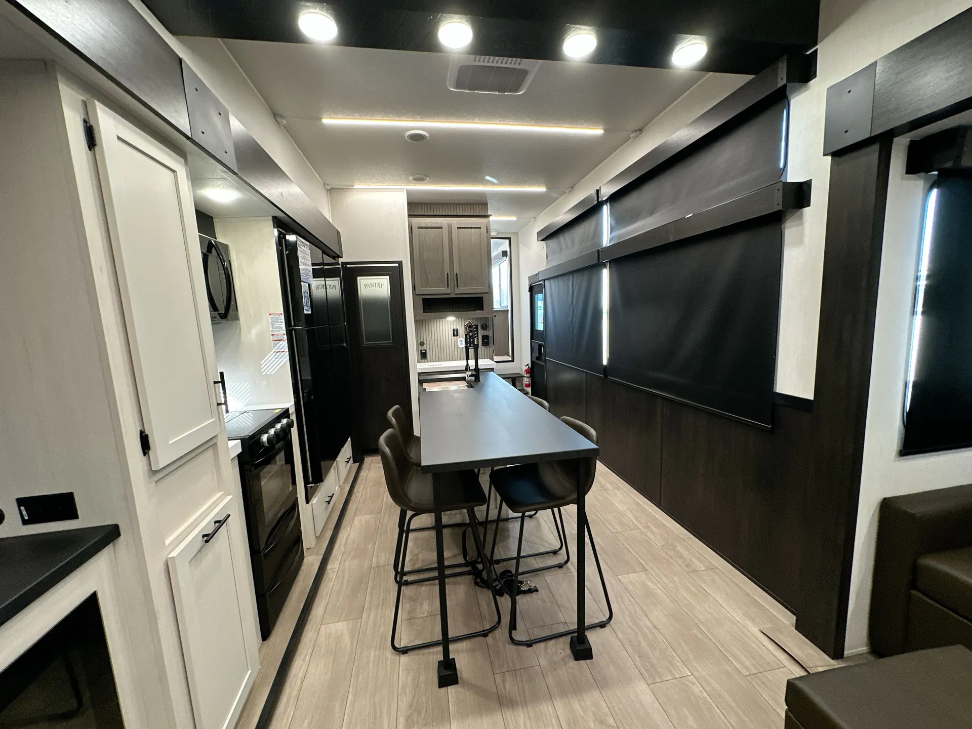 2026 Forest River Arctic Wolf 38LEAH.G — Dining table and chairs centered between the kitchen appliances and cabinetry, with lounge seating visible at the edge