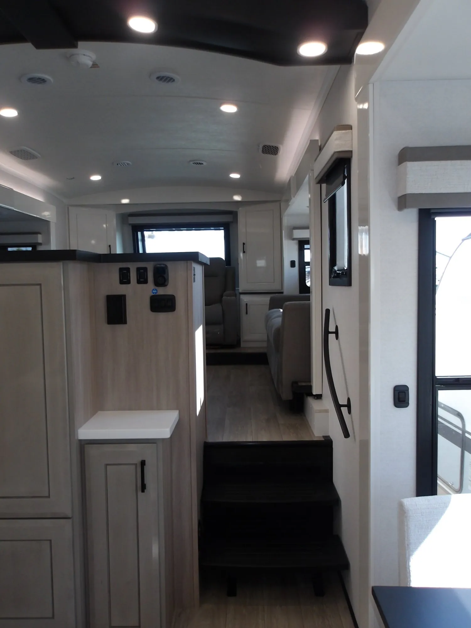 2027 Jayco Pinnacle 39FLOK — Fifth-wheel interior aisle showing kitchen cabinetry in front and a raised lounge with recliners beyond