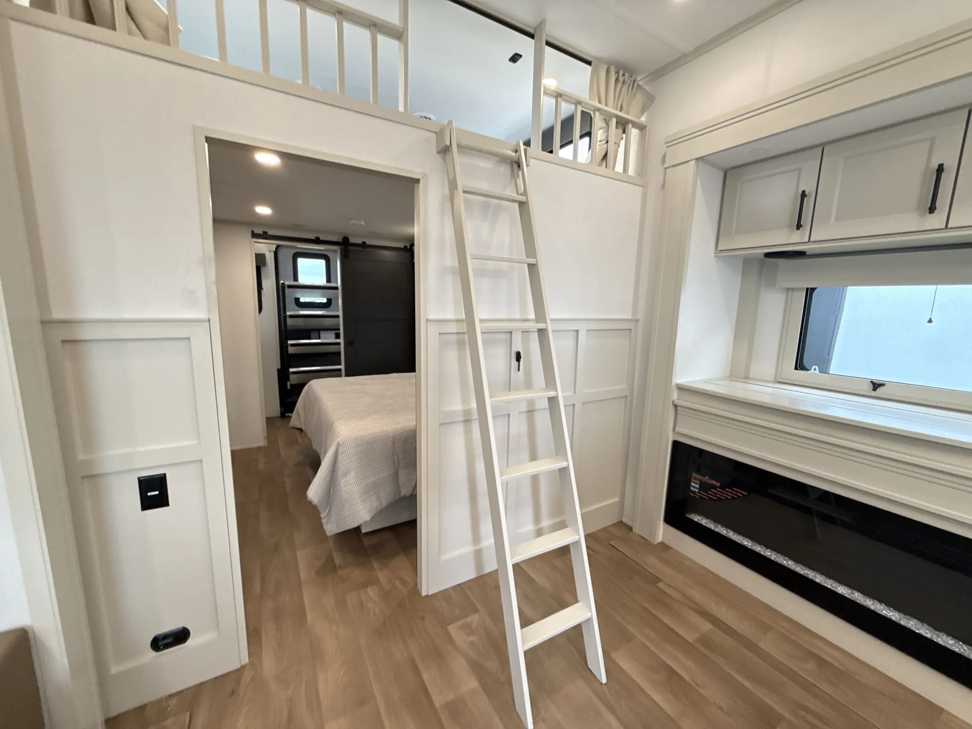 2026 Grand Design Solitude 391DL — Elevated loft with ladder above a main bedroom doorway, overlooking a living area fireplace