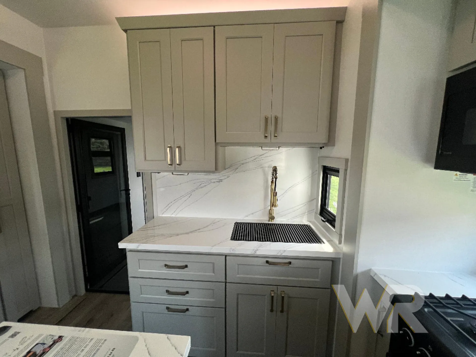 2026 Brinkley Model G 3950 — Kitchen sink and spring faucet set into a marble-pattern countertop beneath upper cabinets beside a gas range