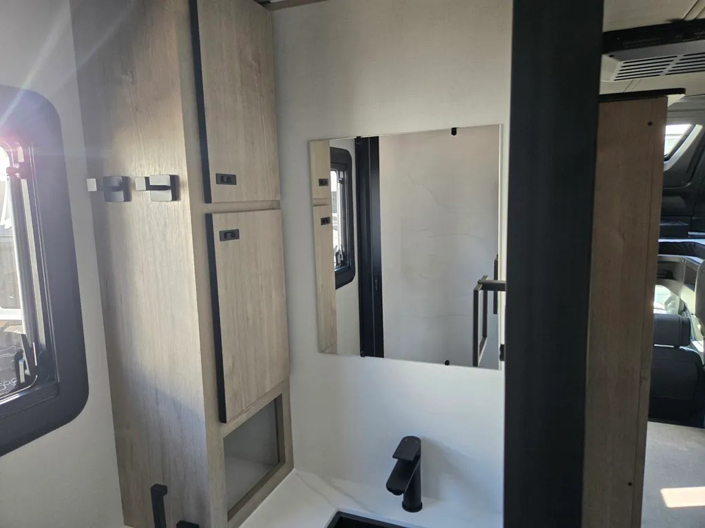 2027 Grand Design Lineage Series F 29AN5 — Bathroom vanity with black faucet, wall mirror, light wood cabinets, and a partial view toward the cab