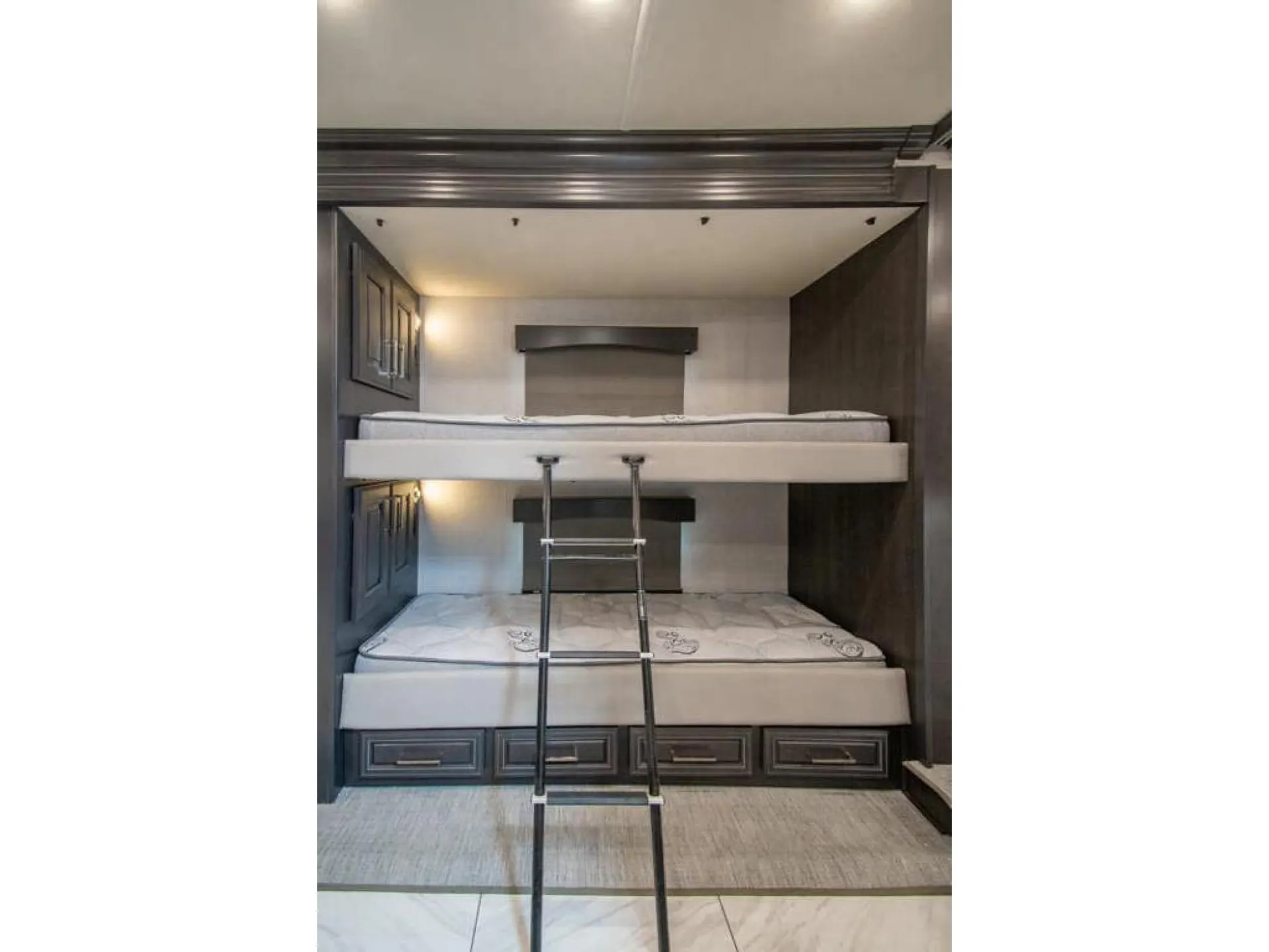 2026 Fleetwood Discovery LXE 40G — Bunk sleeping area with two stacked mattresses, a central ladder, surrounding cabinets, and lower storage drawers