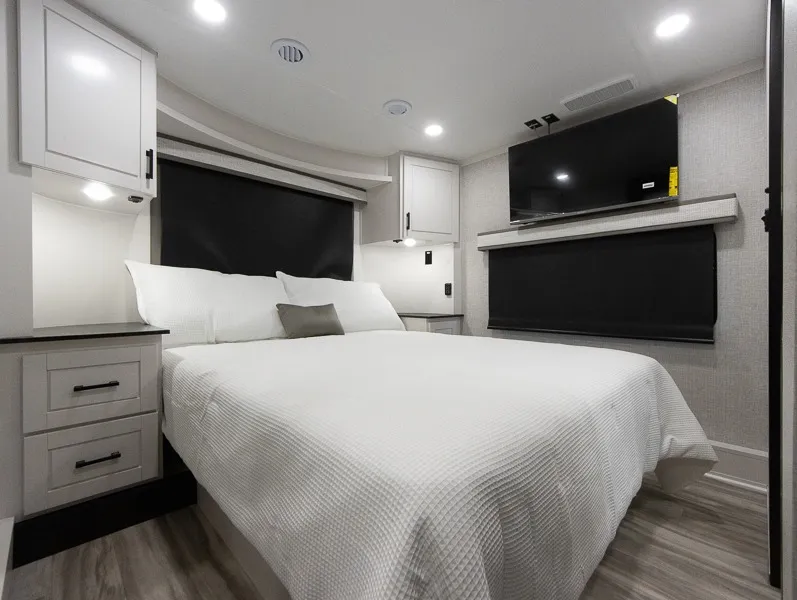2025 Jayco Seismic Luxury Series 4113 — Main bedroom with a bed, bedside drawers, overhead cabinets, windows, and wall-mounted television