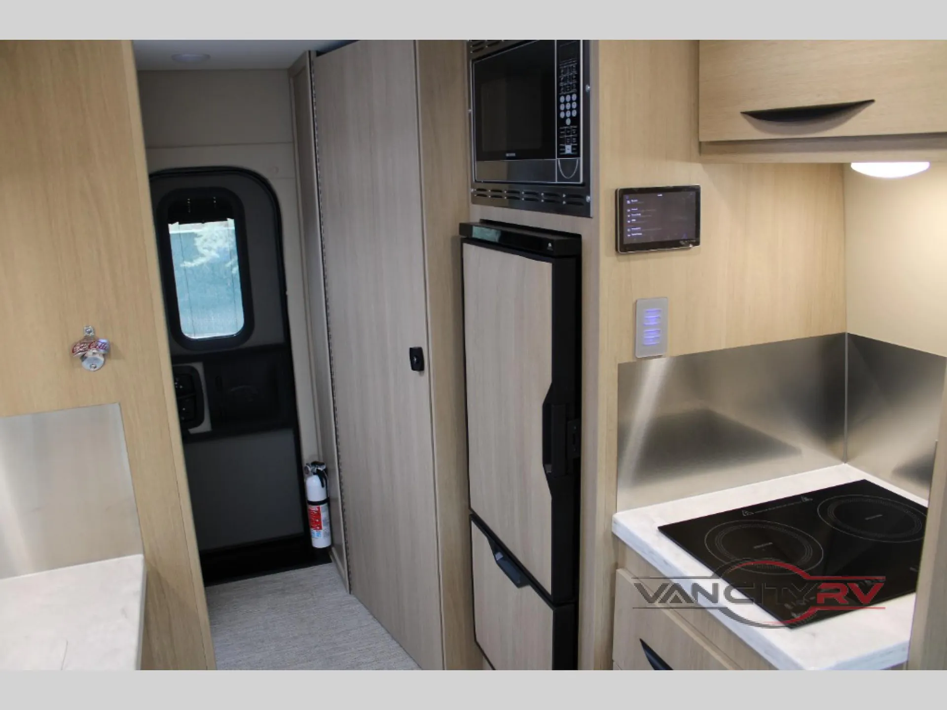 2025 Chinook RV Maverick SS — Van kitchen with induction cooktop, refrigerator, microwave, cabinetry, and stainless backsplash beside the entry door