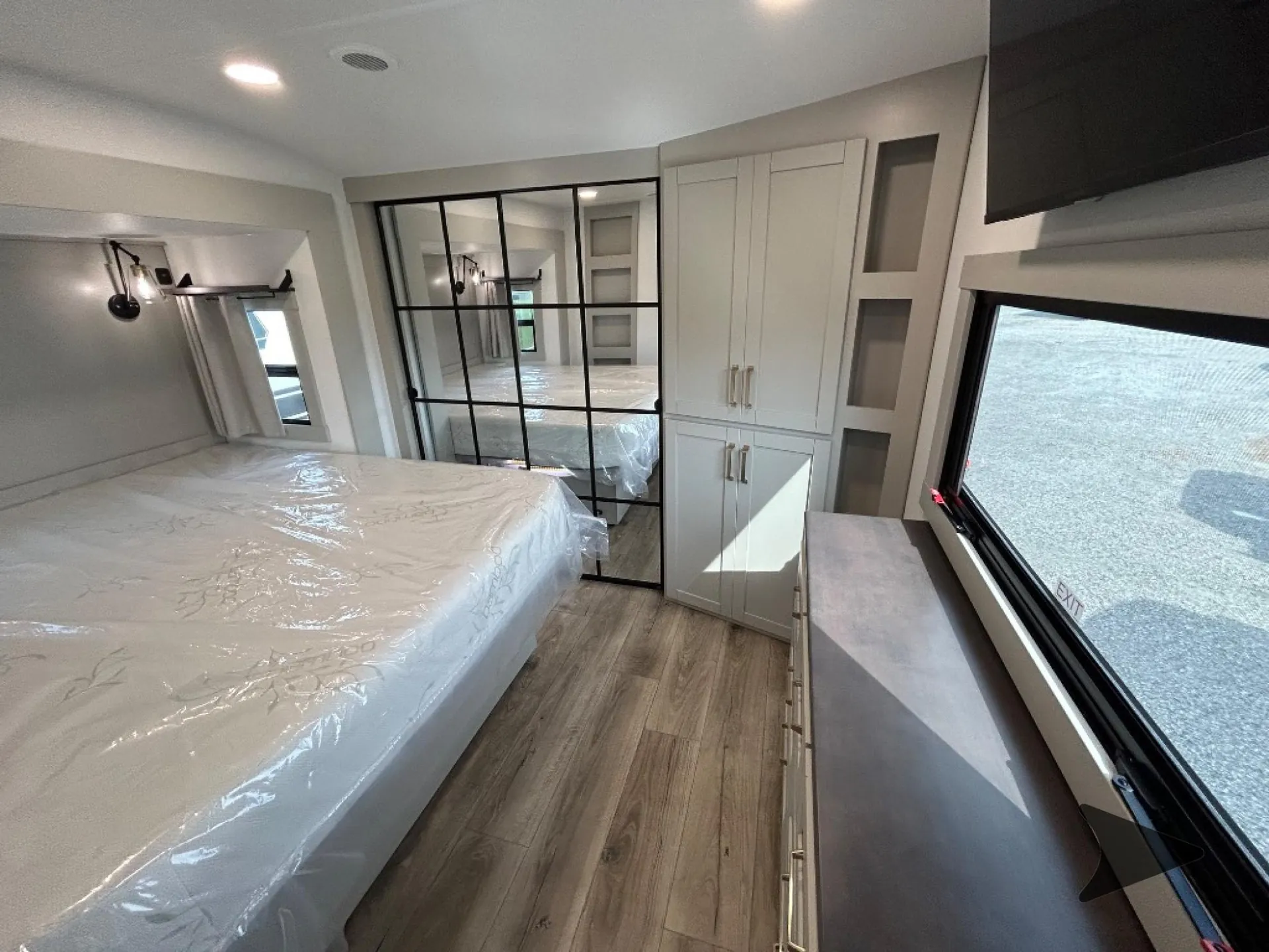 2026 Brinkley Model Z 3515 — Main bedroom with a plastic-wrapped bed, wardrobe cabinets, dresser, window, and mirrored sliding partition