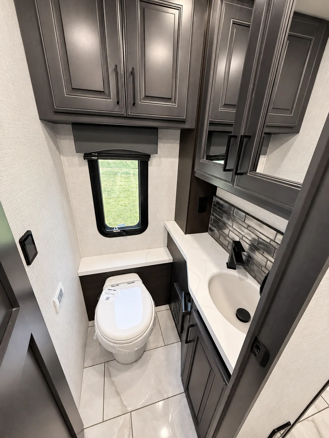 2027 Fleetwood Discovery LXE 40M — Bathroom with toilet, vanity sink, backsplash, mirrored cabinetry, window, and lower storage cabinets