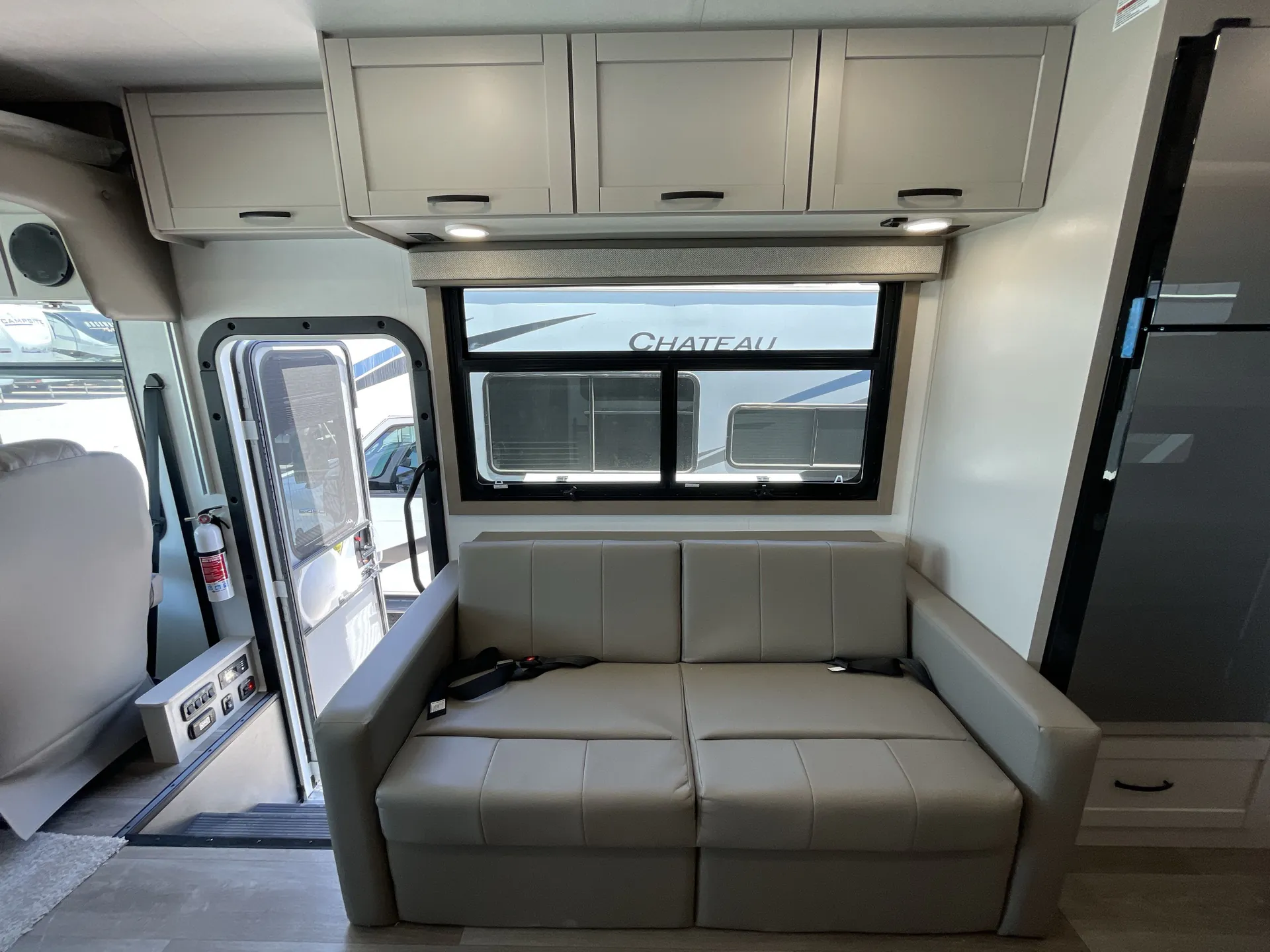 2027 Jayco Alante 29F — Foldable living-room sofa beneath a window and overhead cabinets beside the entry door