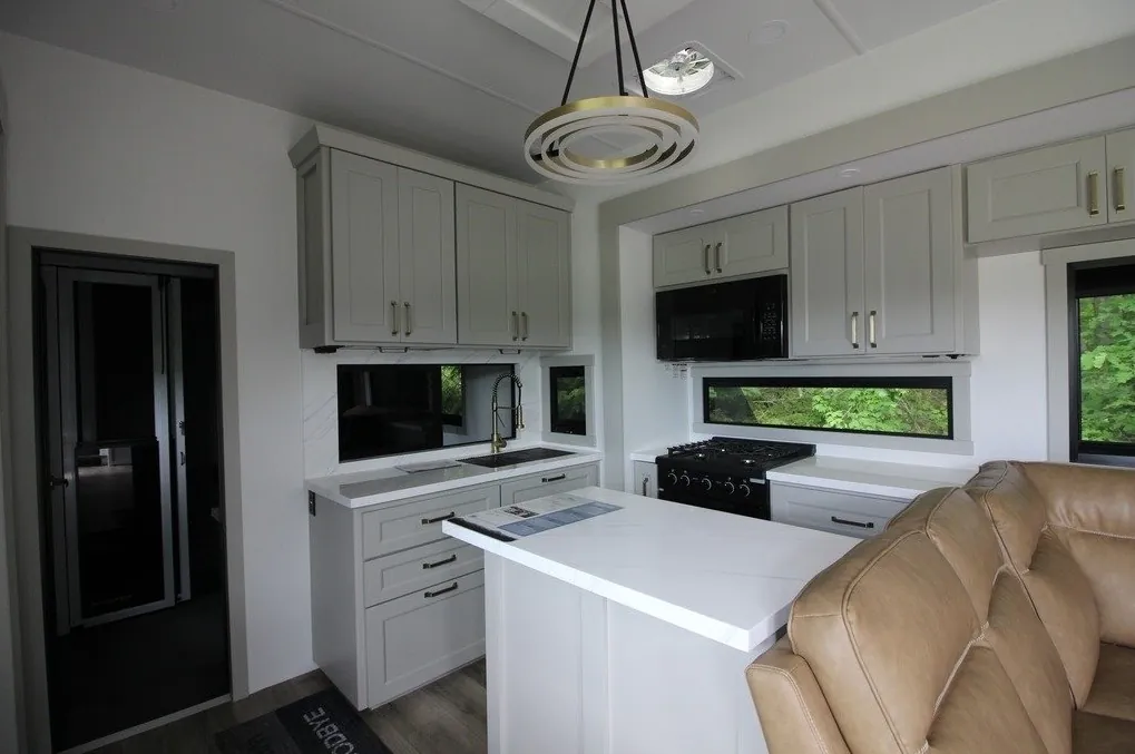 2025 Brinkley Model G 3250 — Fifth wheel kitchen with island, sink, range, microwave, cabinetry, and a leather sofa at right