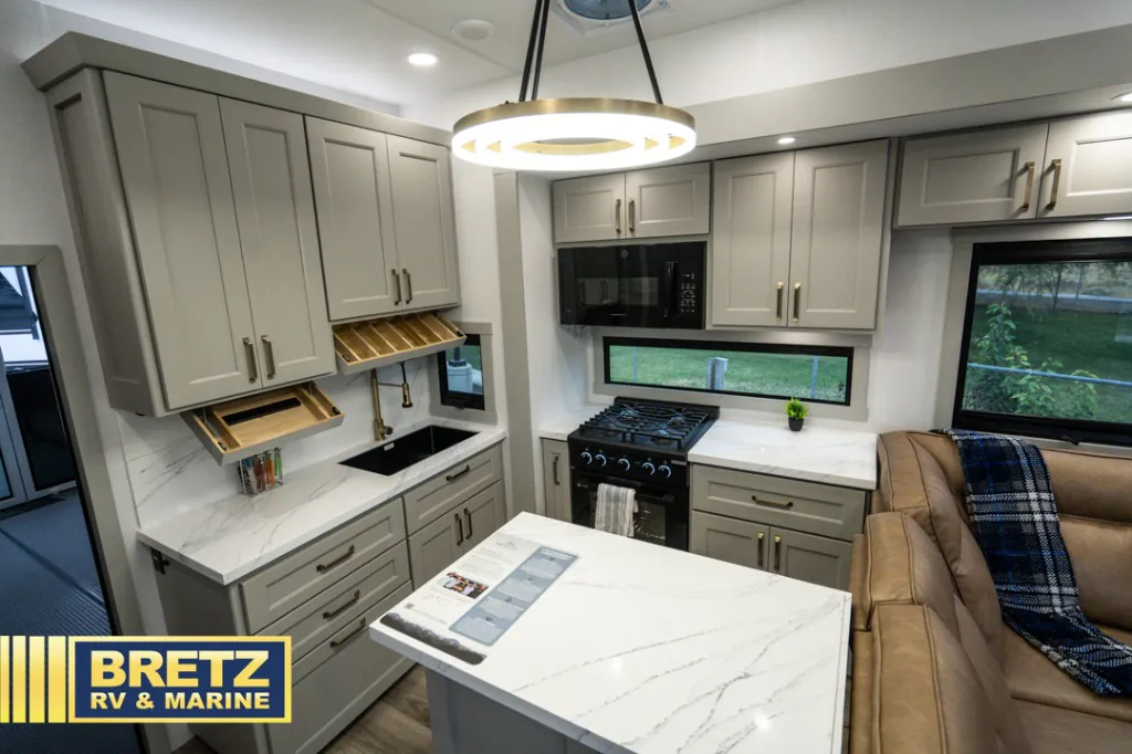 2026 Brinkley Model G 3950 — Fifth wheel kitchen with sink, range, microwave, island, cabinetry, and a leather sofa beside the counter
