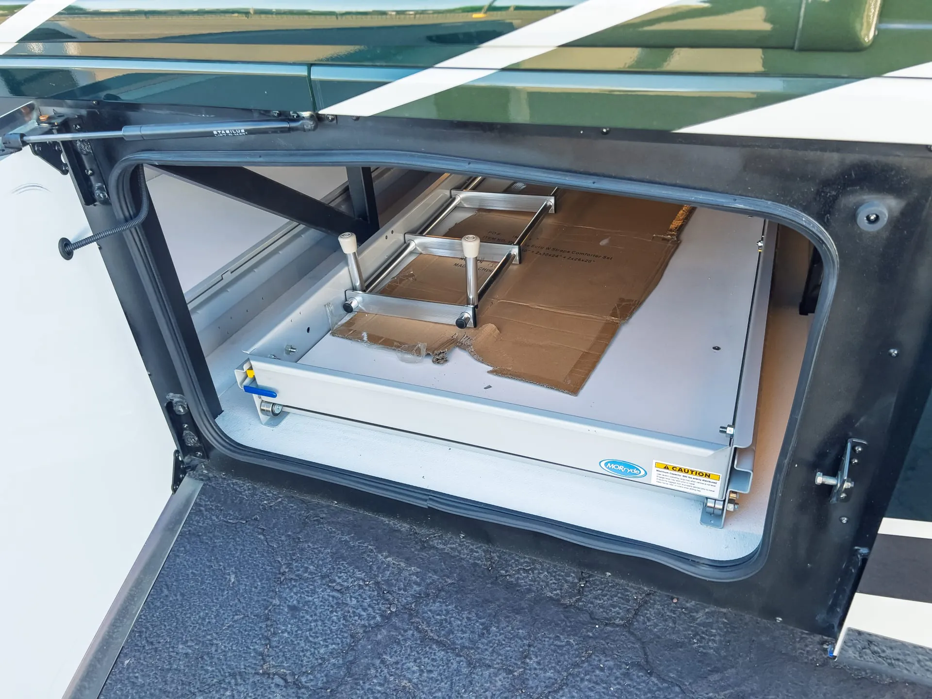 2027 Fleetwood Discovery LXE 40M — Open exterior bay visibly shows a storage slide tray and stored packaging