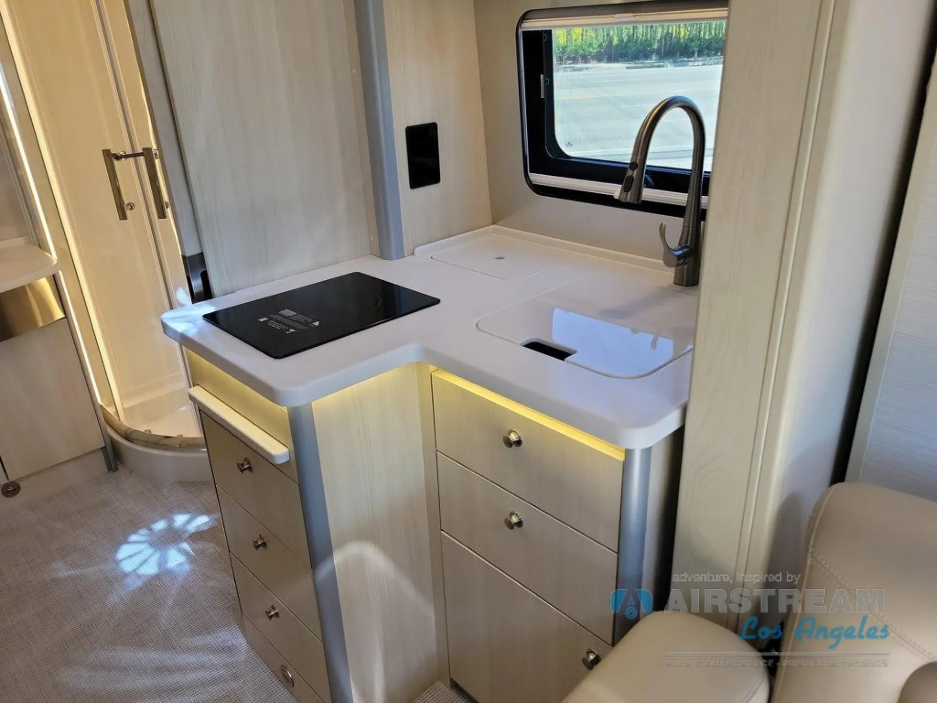 2026 Airstream Atlas Murphy Suite — Class B kitchen with induction cooktop, sink, faucet, drawers, and a curved shower enclosure behind it