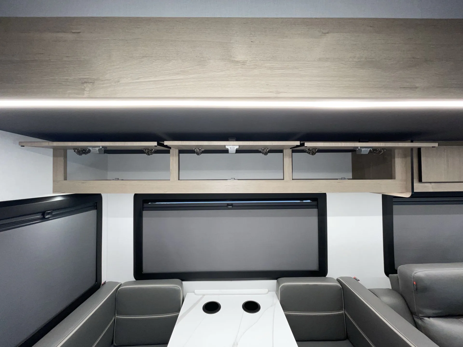 2027 Grand Design Lineage Series F 31ZW — White dining table with cupholders sits between booth seats, with lounge recliners visible at right