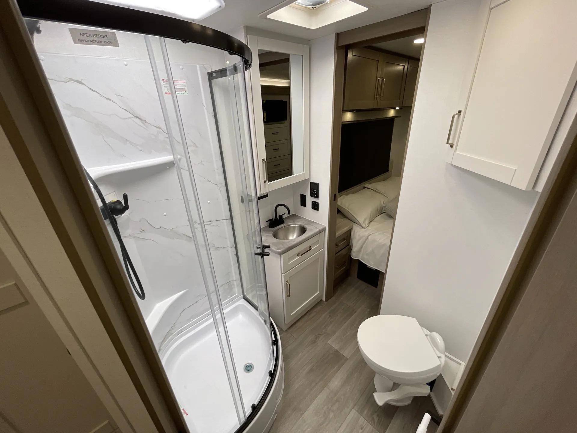 2027 Jayco Alante 29F — Bathroom overview with curved shower, toilet, vanity, and an open view into the adjacent bedroom