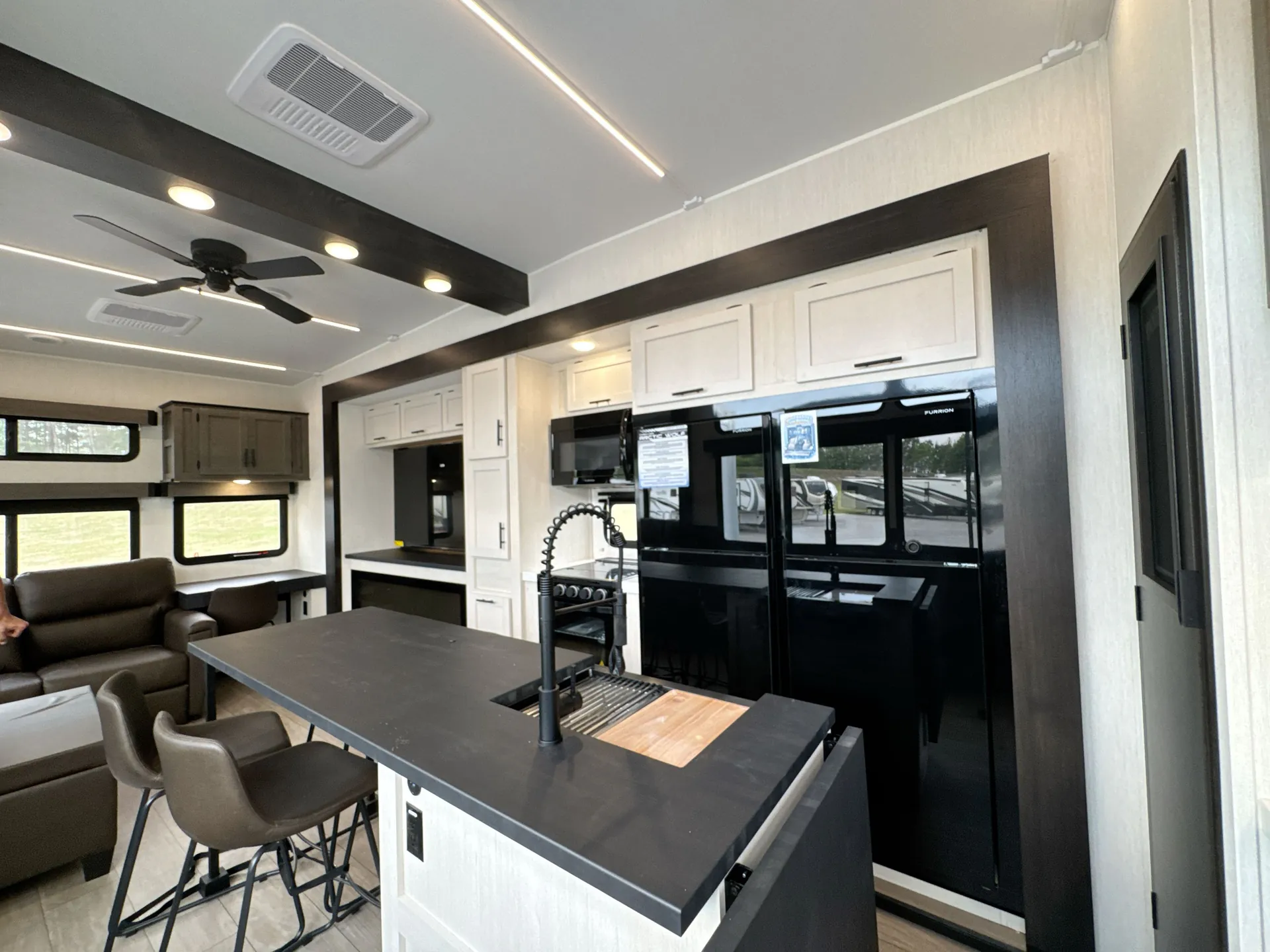 2026 Forest River Arctic Wolf 38LEAH.G — Fifth-wheel kitchen island with sink facing the dining table, with sofas and entertainment cabinetry visible beyond
