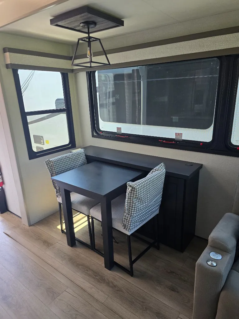 2026 Jayco North Point 377RLBH — Dining area with a small table and two chairs beside a living-area recliner and surrounding windows