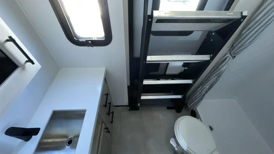 2026 Grand Design Solitude 391DL — Bathroom with vanity sink, toilet, shower ladder, skylight, and wall cabinetry visible together