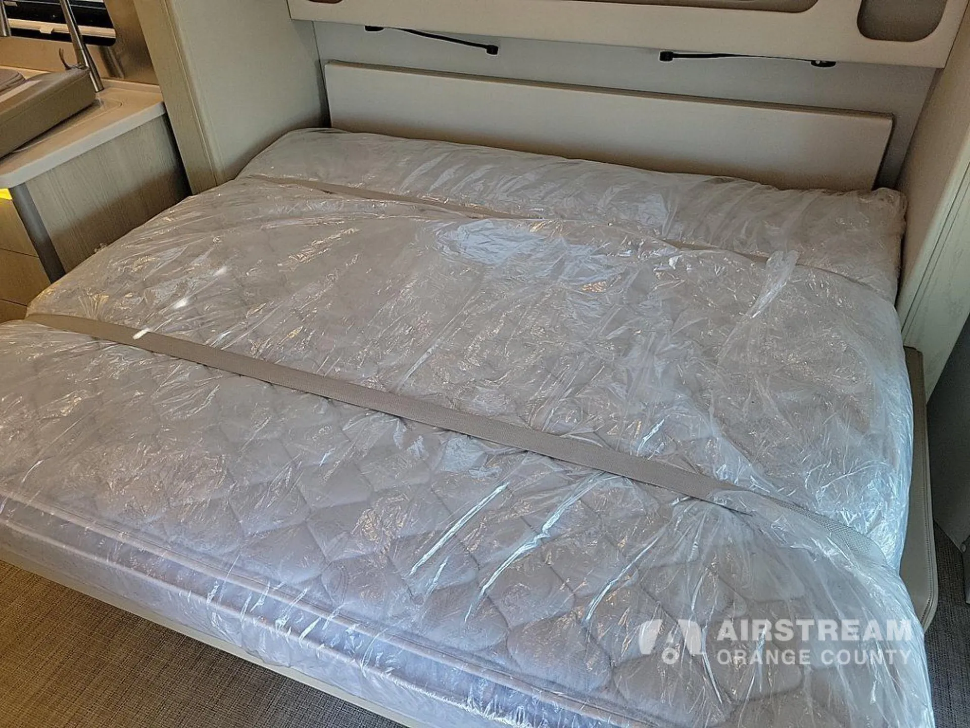 2026 Airstream Atlas Murphy Suite — Main bed covered in protective plastic with a headboard and overhead cabinetry visible