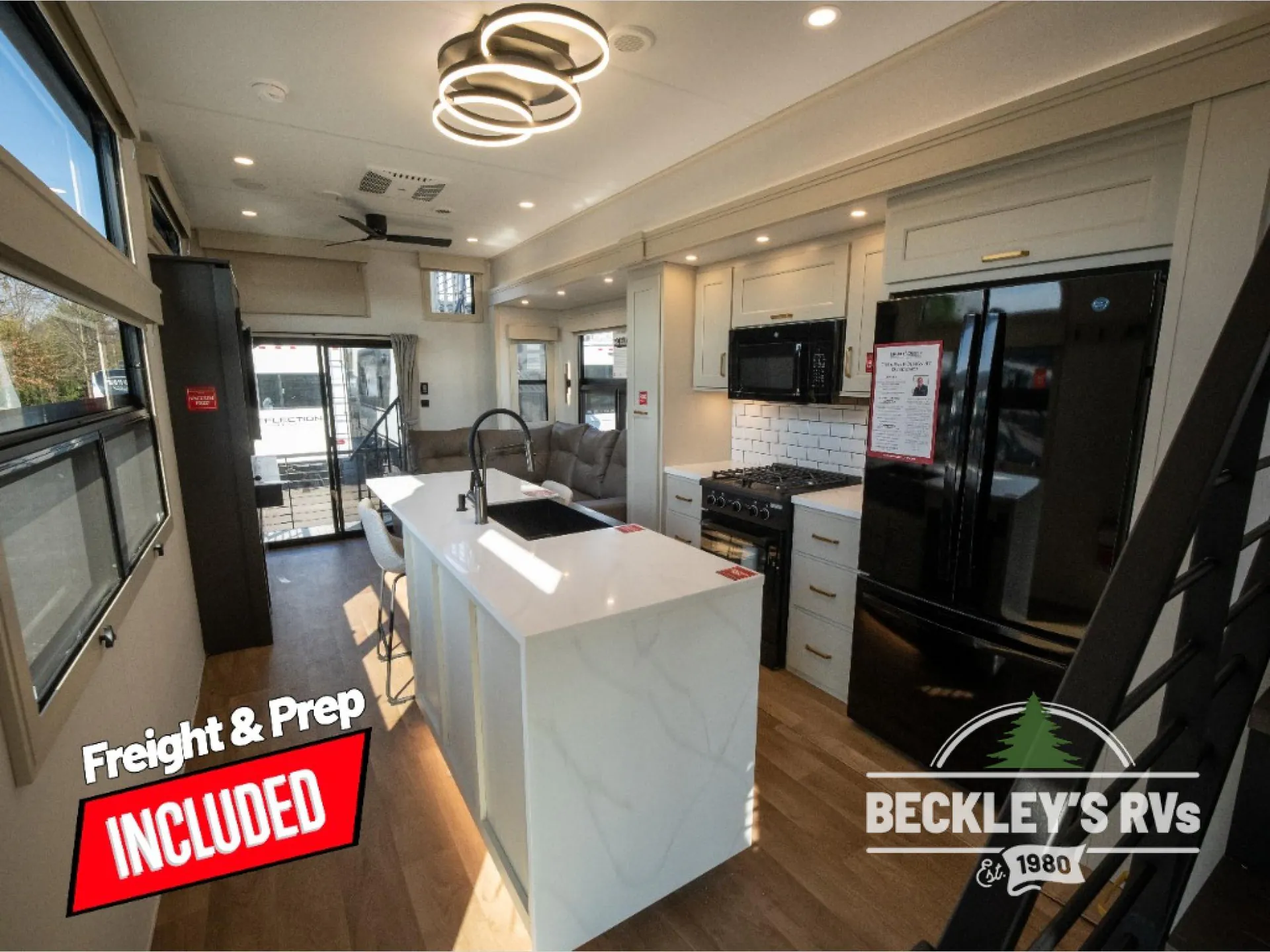 2026 Grand Design Foundation 42GD — Large kitchen island with sink facing a range and refrigerator, with a sofa and dining stools beyond