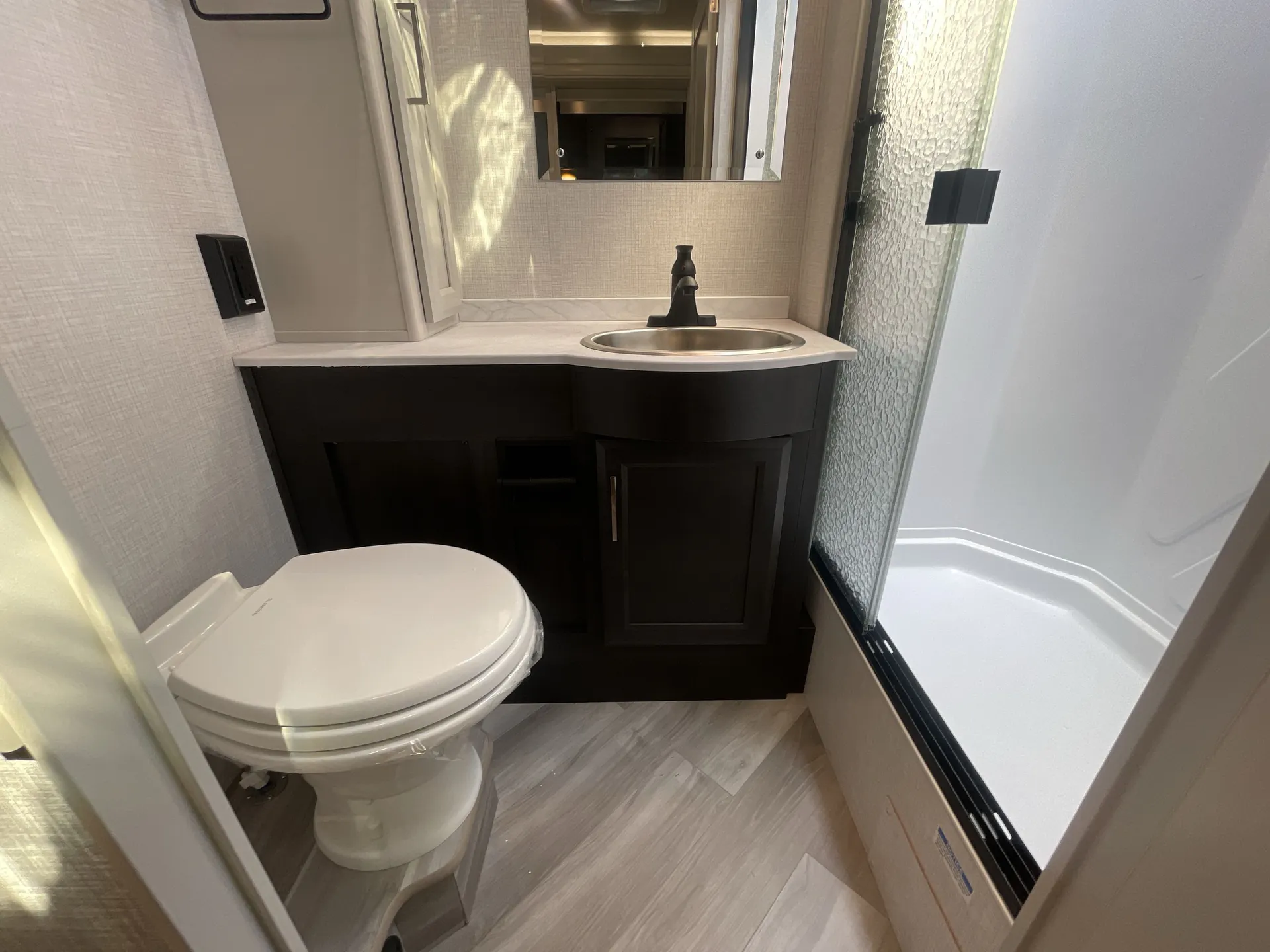 2026 Holiday Rambler Invicta 36Y — RV bathroom with toilet, dark vanity, oval sink, mirror, and glass-enclosed shower