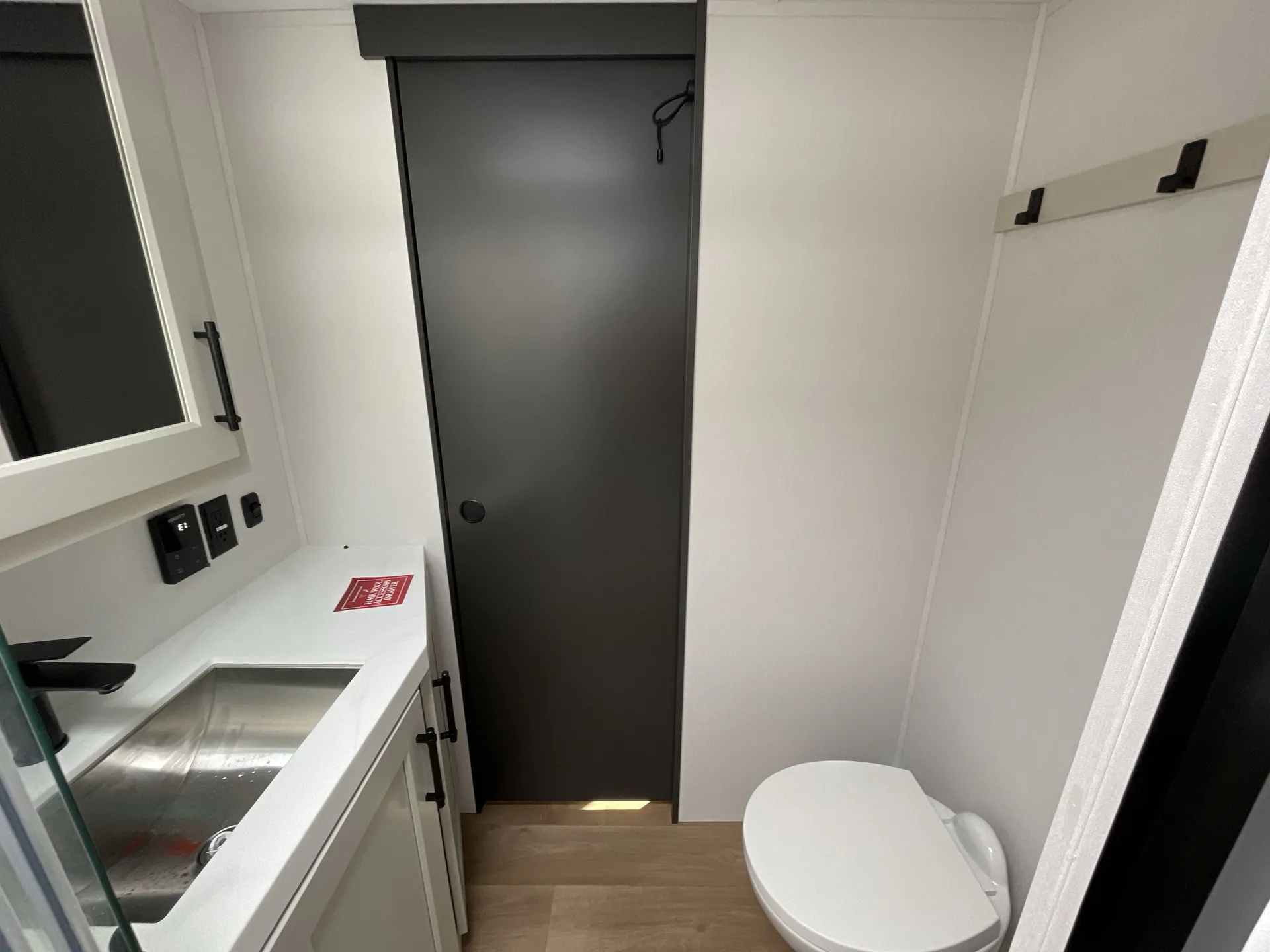 2026 Grand Design Solitude 391DL — Bathroom corner with a vanity sink, toilet, mirrored cabinet, control panel, and closed interior door