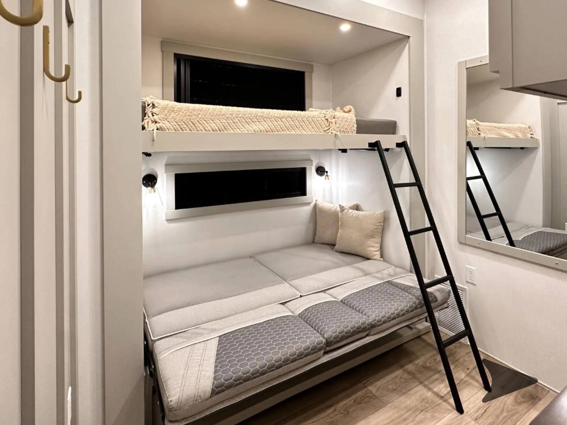 2026 Brinkley Model Z 3610 — Elevated sleeping platform with ladder above a sofa, wall lighting, windows, and mirrored cabinetry