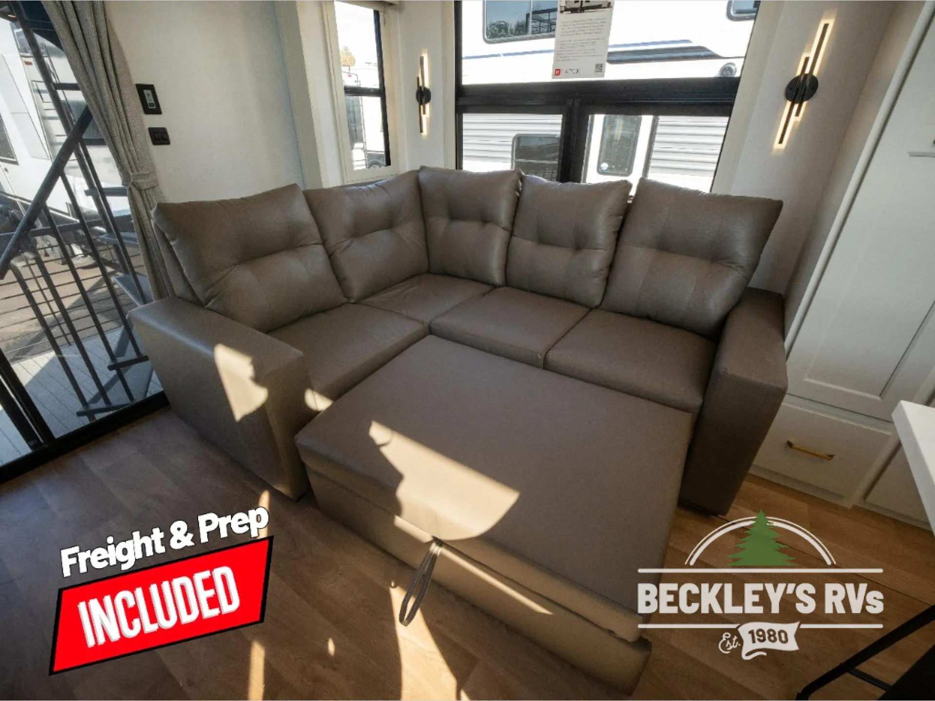 2026 Grand Design Foundation 42GD — Large upholstered sectional sofa with chaise fills the destination trailer lounge beside windows and a stair rail