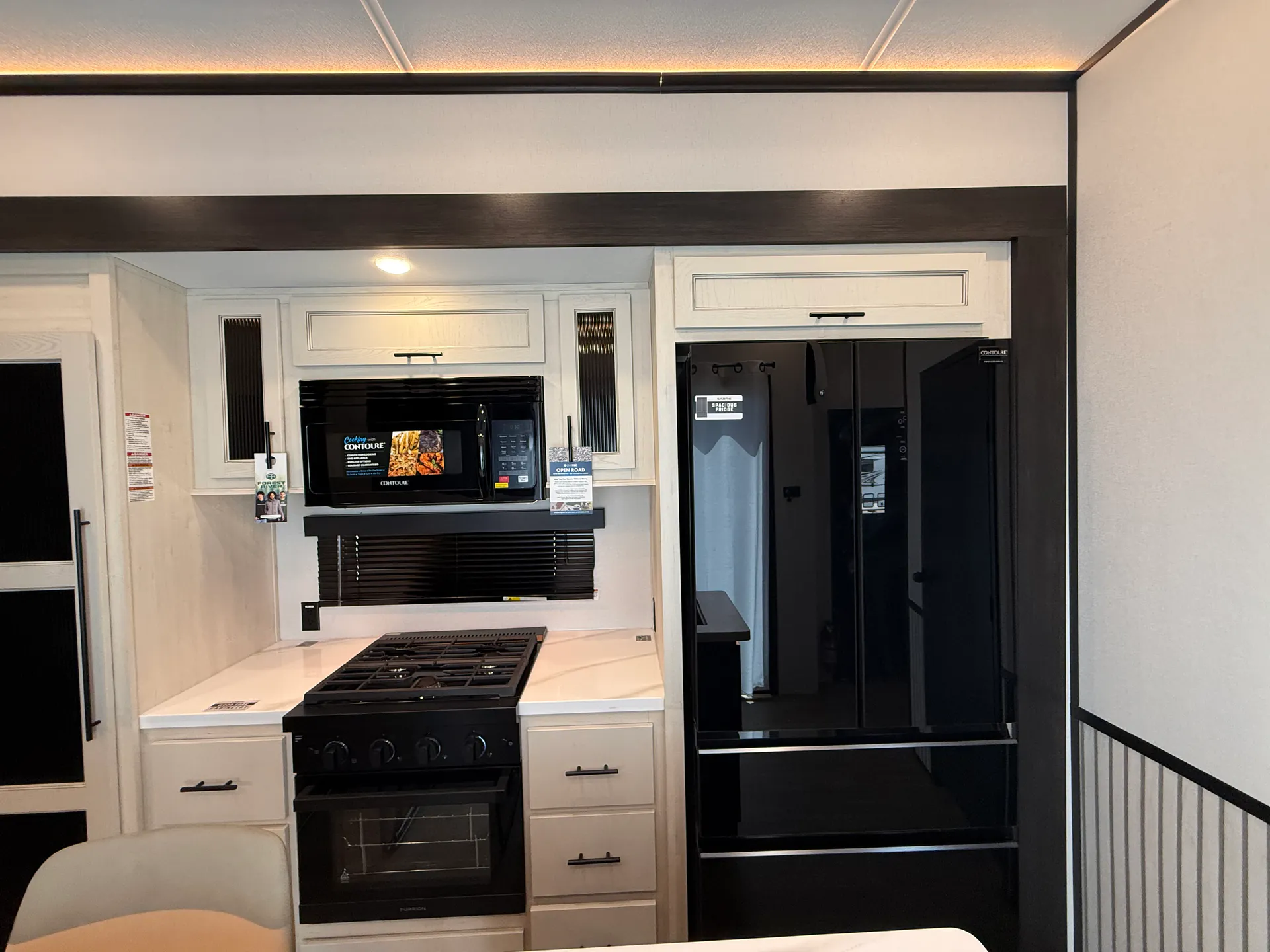2027 Forest River Sabre 38RVHUNTER — Fifth wheel kitchen showing the range, oven, microwave, white counters, cabinetry, and full-height refrigerator