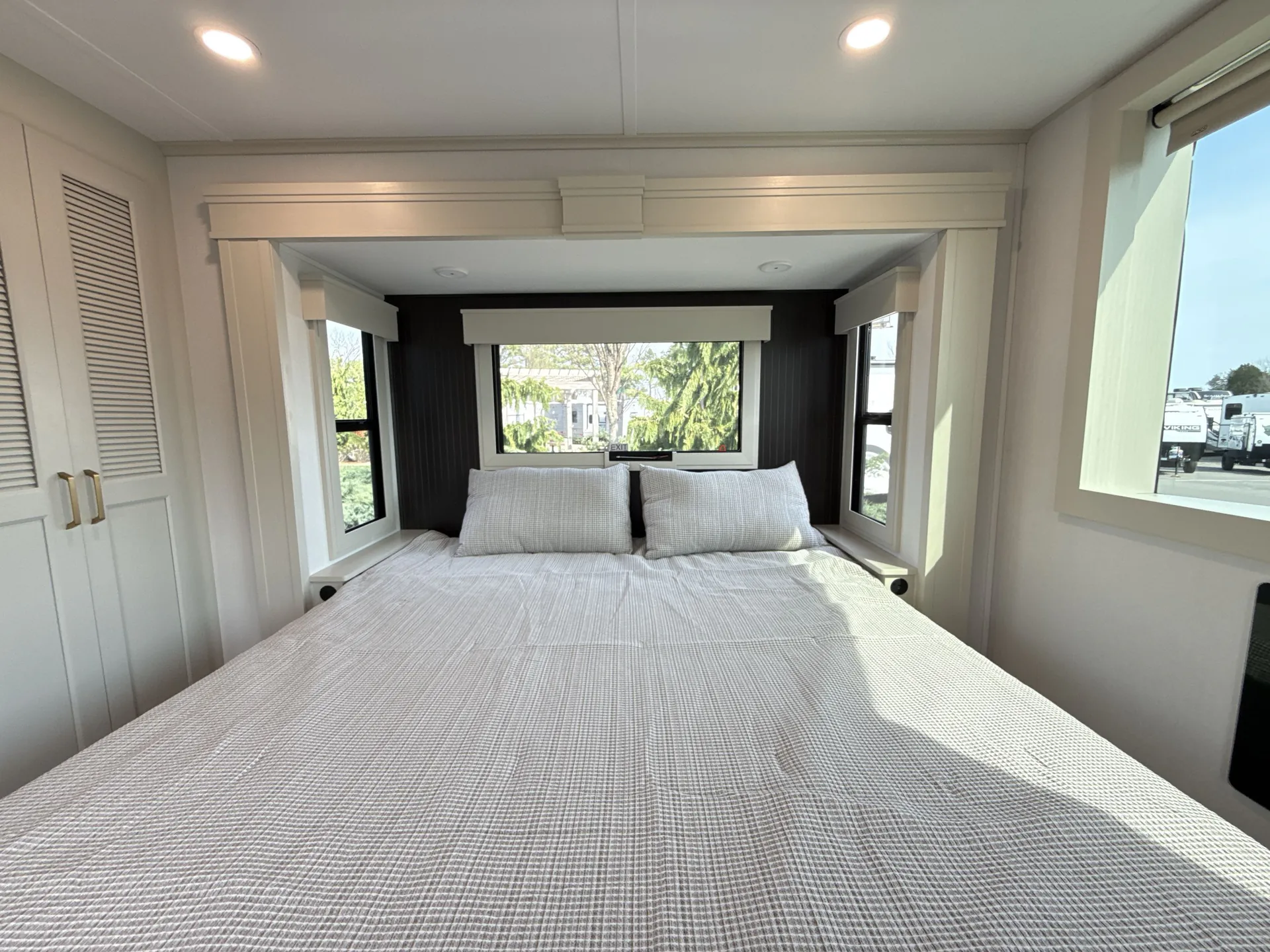 2026 Grand Design Foundation 42GD — Main bedroom centered on a made bed beneath a wide window, with side windows and wardrobe doors