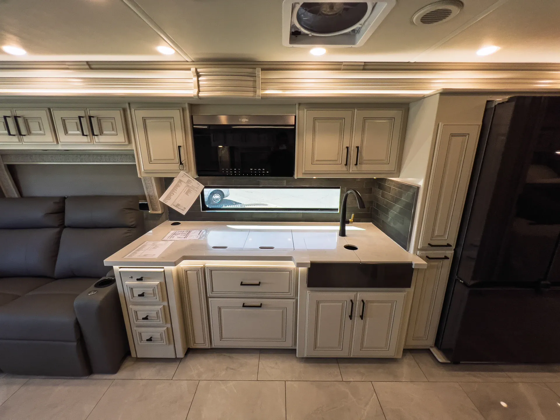 2027 Fleetwood Discovery LXE 40M — Class A kitchen with sink, induction cooktop, microwave, cabinets, and adjacent recliner