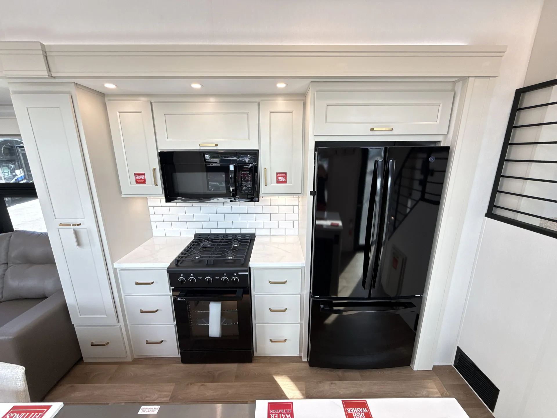 2026 Grand Design Foundation 42GD — Destination trailer kitchen wall with a gas range, microwave, refrigerator, white cabinetry, drawers, and subway tile backsplash