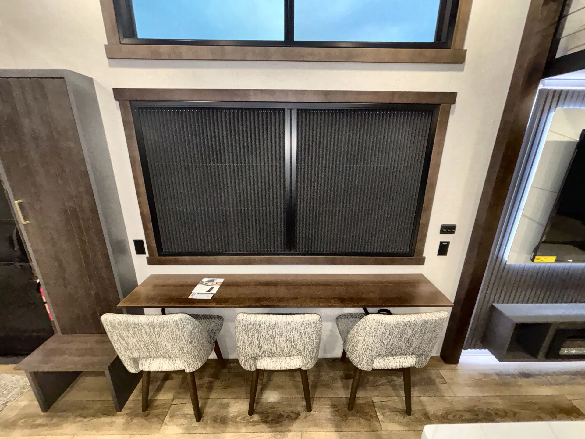 2026 Forest River Cedar Creek Cottage 41FWC — Dining table with three upholstered chairs beneath windows, flanked by built-in shelving and cabinetry