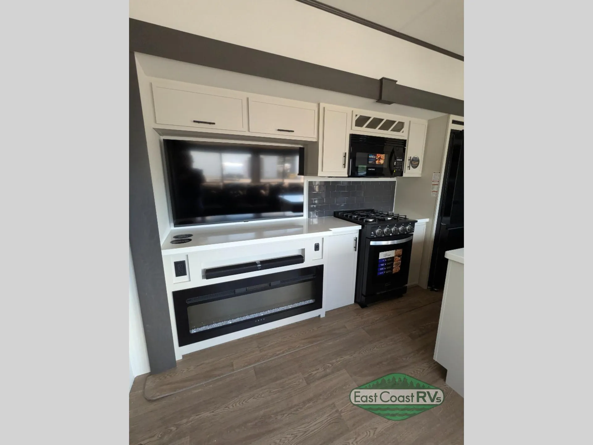 2027 Forest River Sanibel 40BUNK — Fifth wheel living wall with television and fireplace beside a gas range, microwave, backsplash, and surrounding cabinetry
