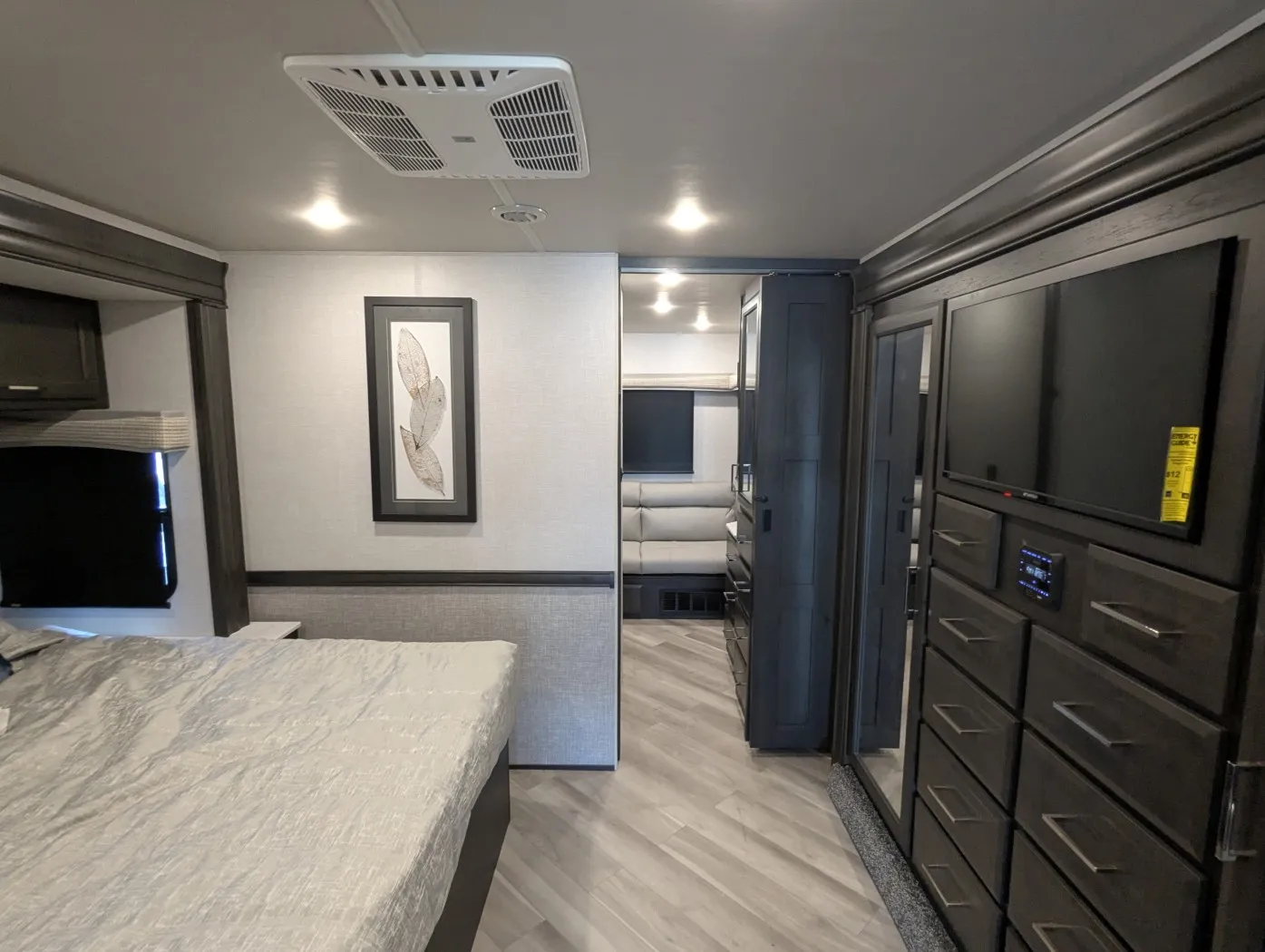 2026 Holiday Rambler Invicta 36Y — Bedroom overview with bed and dresser wall opening toward a separate lounge with reclining seating