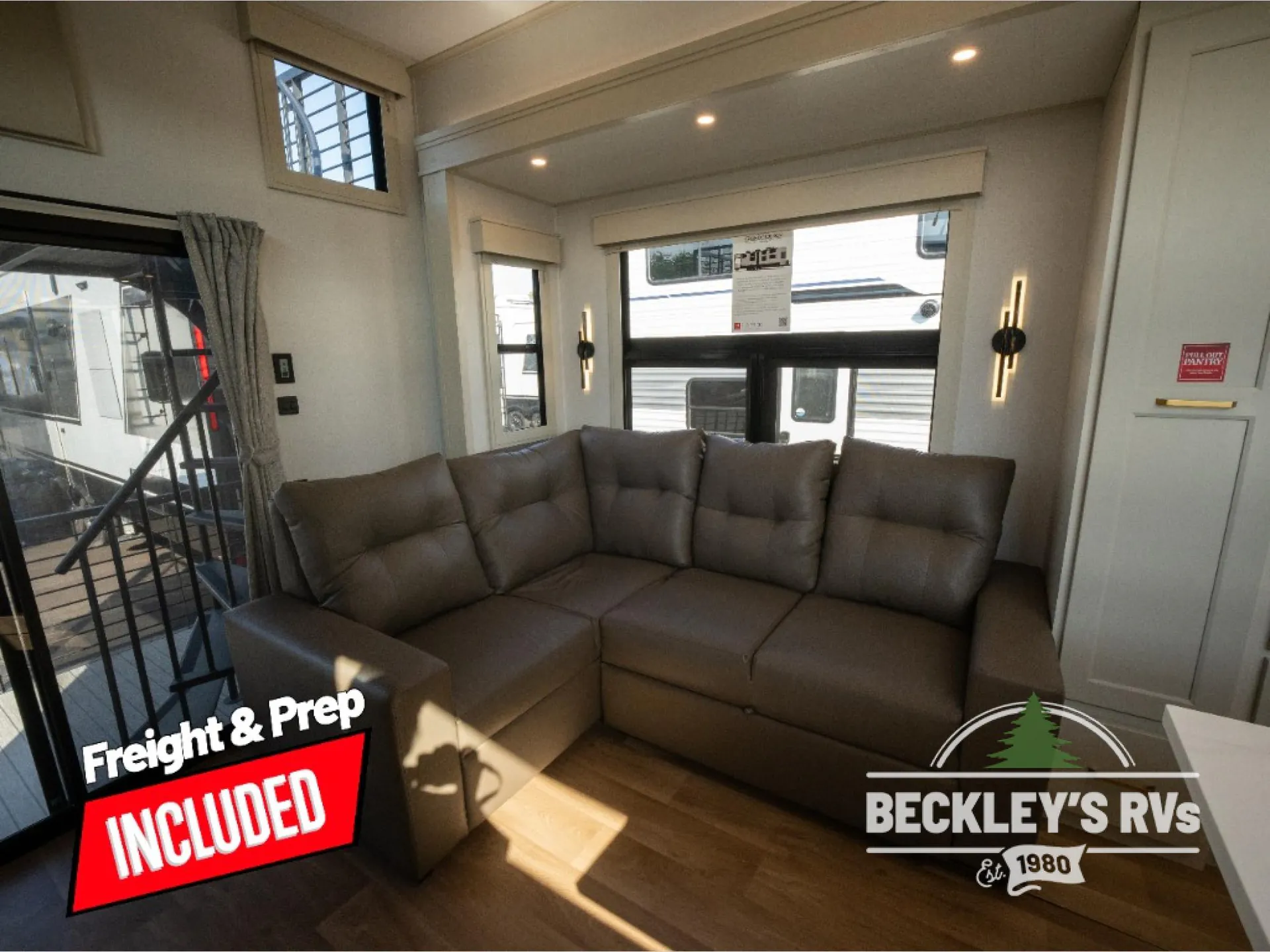 2026 Grand Design Foundation 42GD — Destination trailer living area centered on a large brown sectional beneath wide windows and beside the entry door