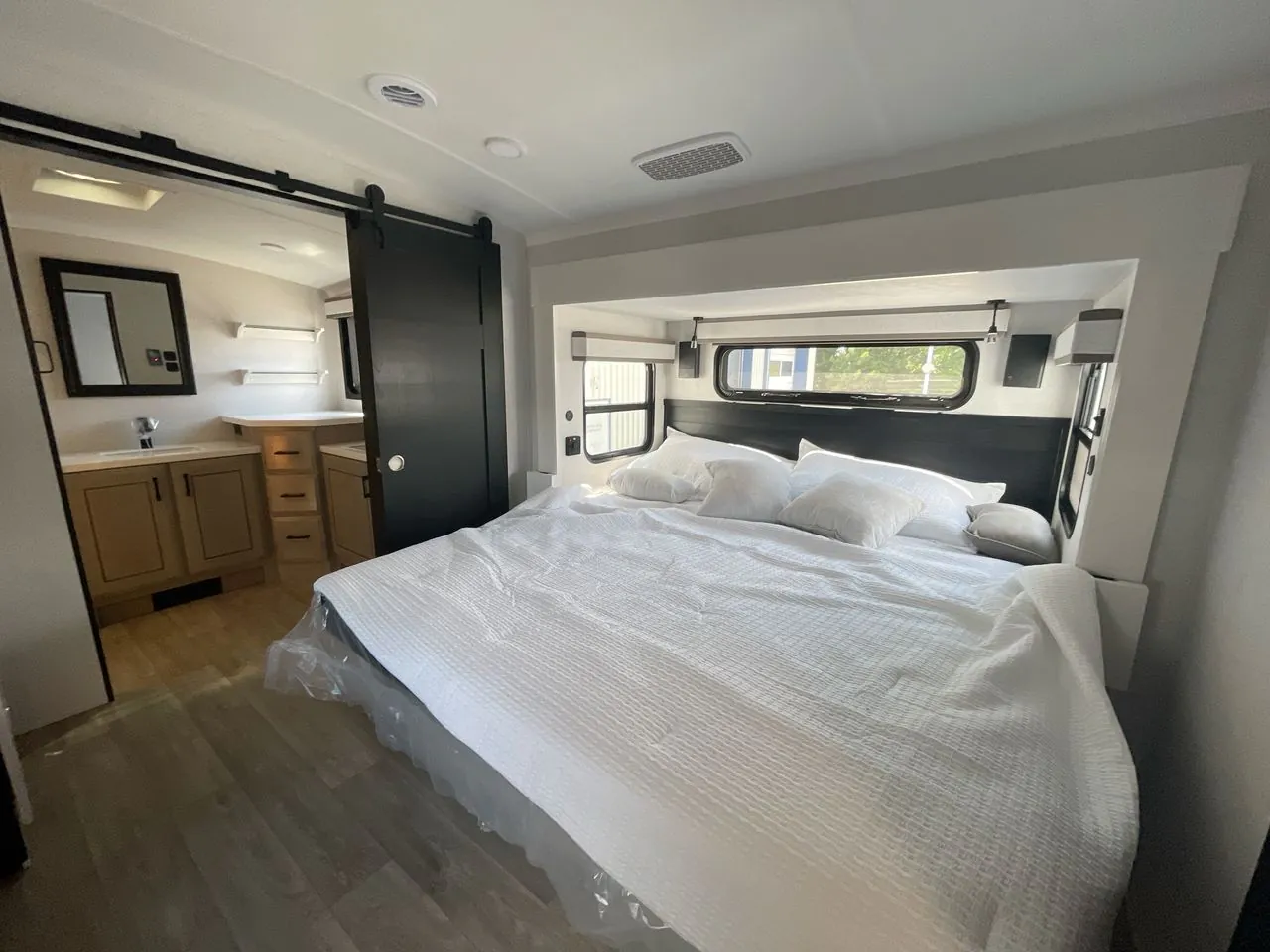 2027 Jayco Pinnacle 39FLOK — Main bedroom with a large bed, wardrobes, dresser, and an adjoining bathroom vanity visible through the doorway