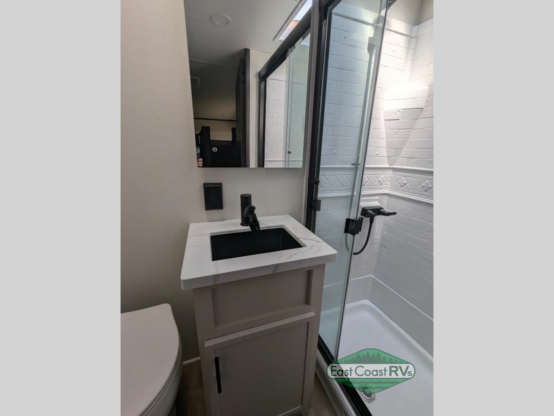 2027 Forest River Sanibel 40BUNK — Bathroom vanity with black sink and mirror beside a glass shower enclosure and partial toilet