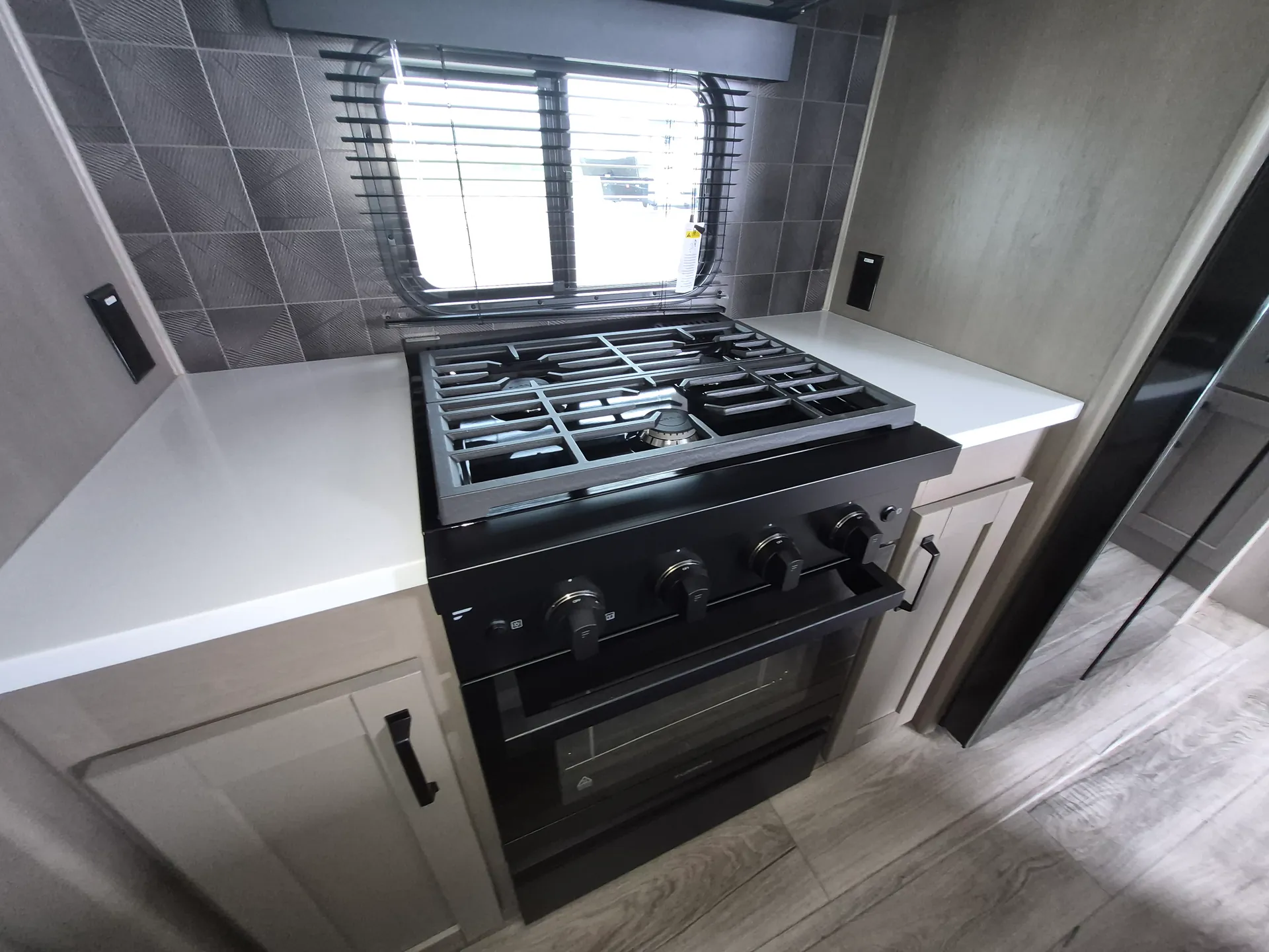 2027 Grand Design Reflection 362TBS — Black range and oven centered between kitchen counters, cabinetry, backsplash, and a window
