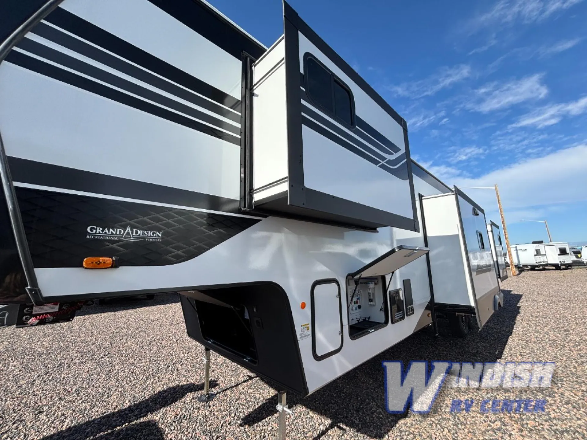 2027 Grand Design Reflection 362TBS — Exterior view of the fifth-wheel showing slide-outs, landing gear, storage doors, and an open utility compartment